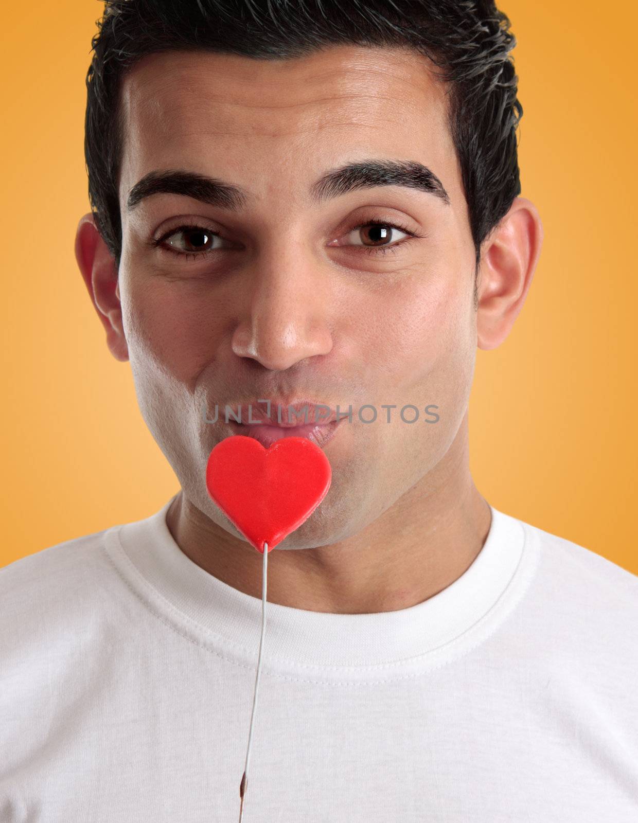 A flirtatious man kissing an edible red love heart on a stick