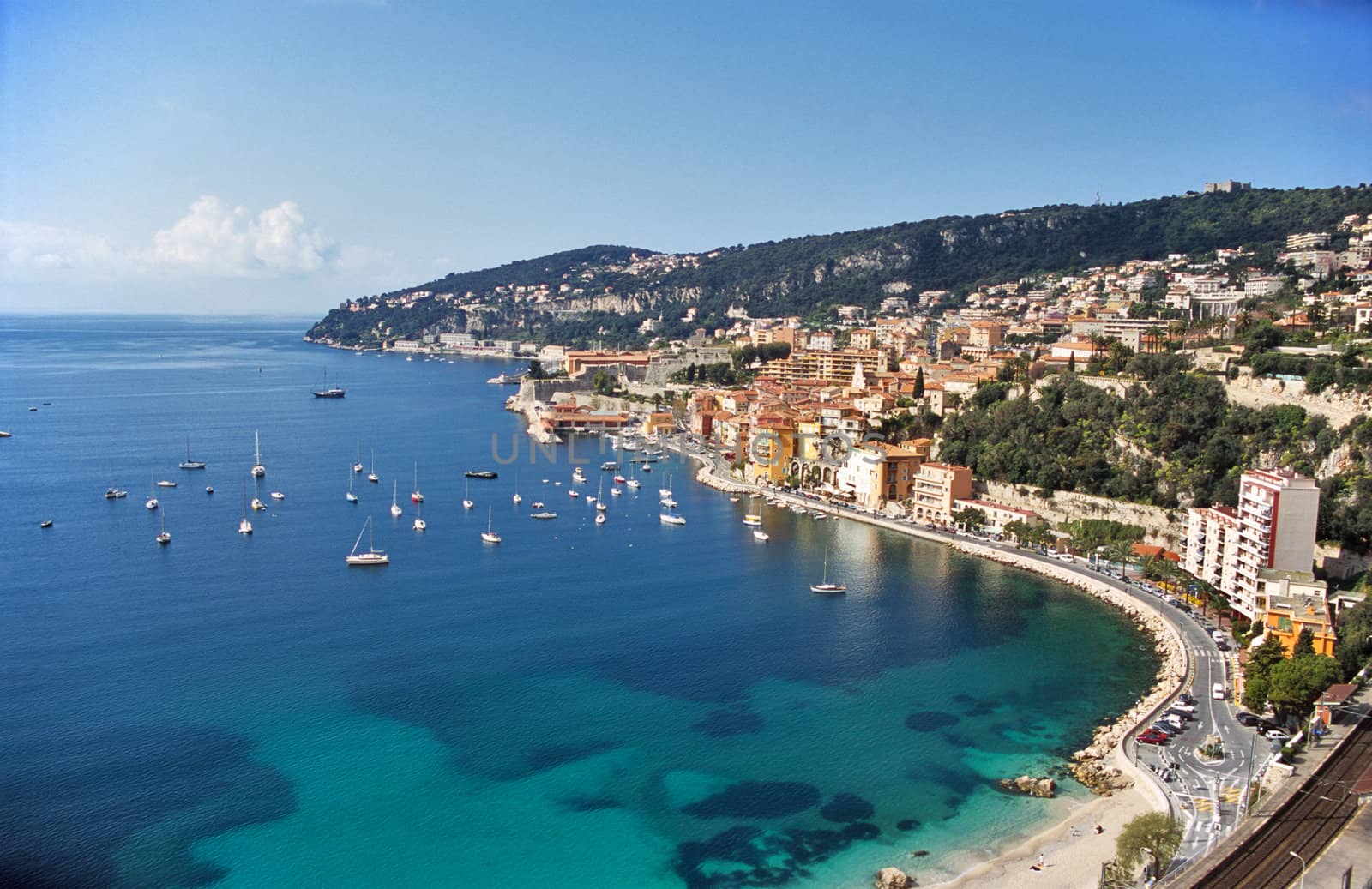 Expensive Condominiums perch on the hillsides above the Mediterranean Sea while sailboats dot the harbour.