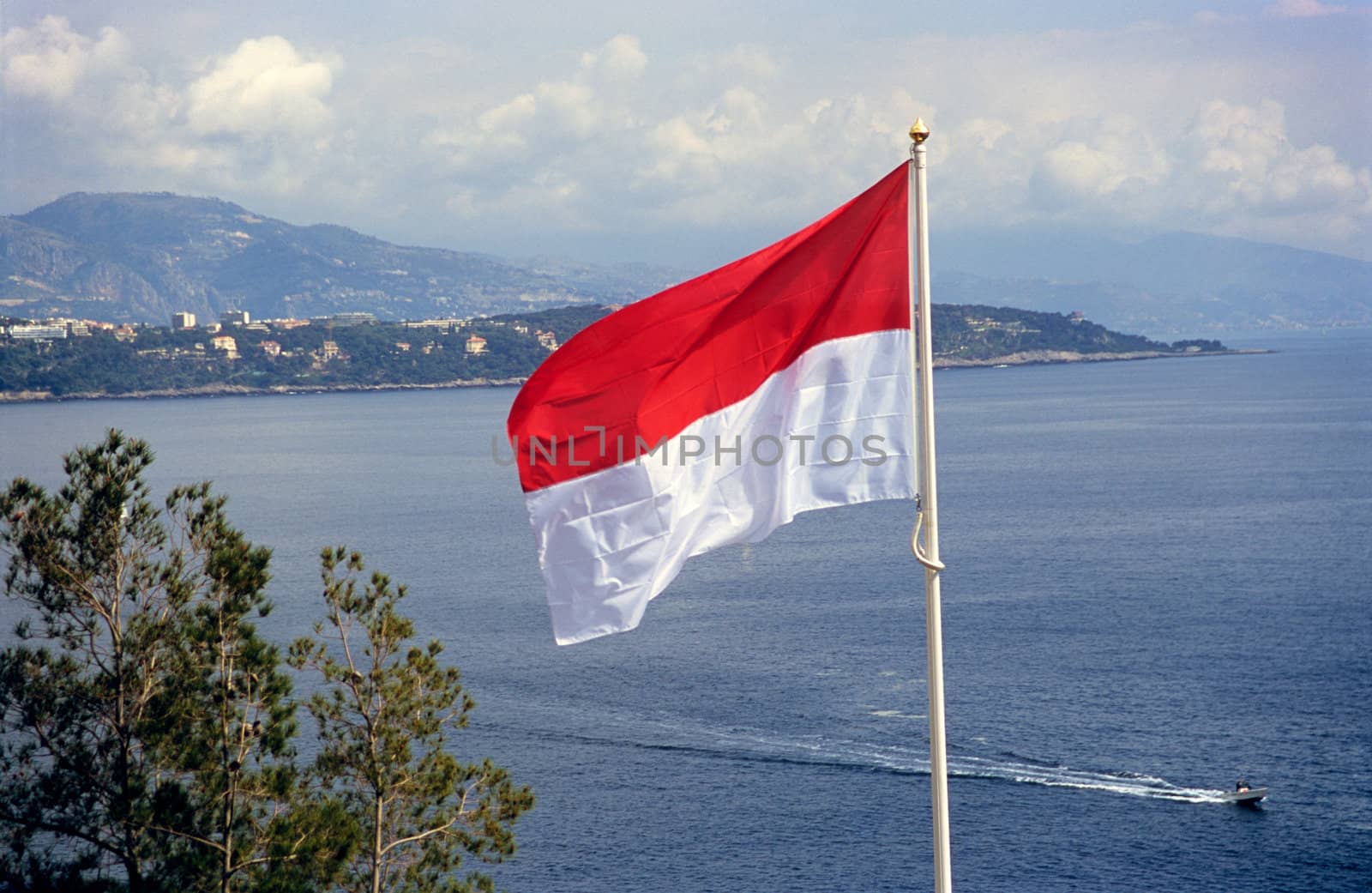 The flag of the principality of Monaco flying over the Mediterranean sea.