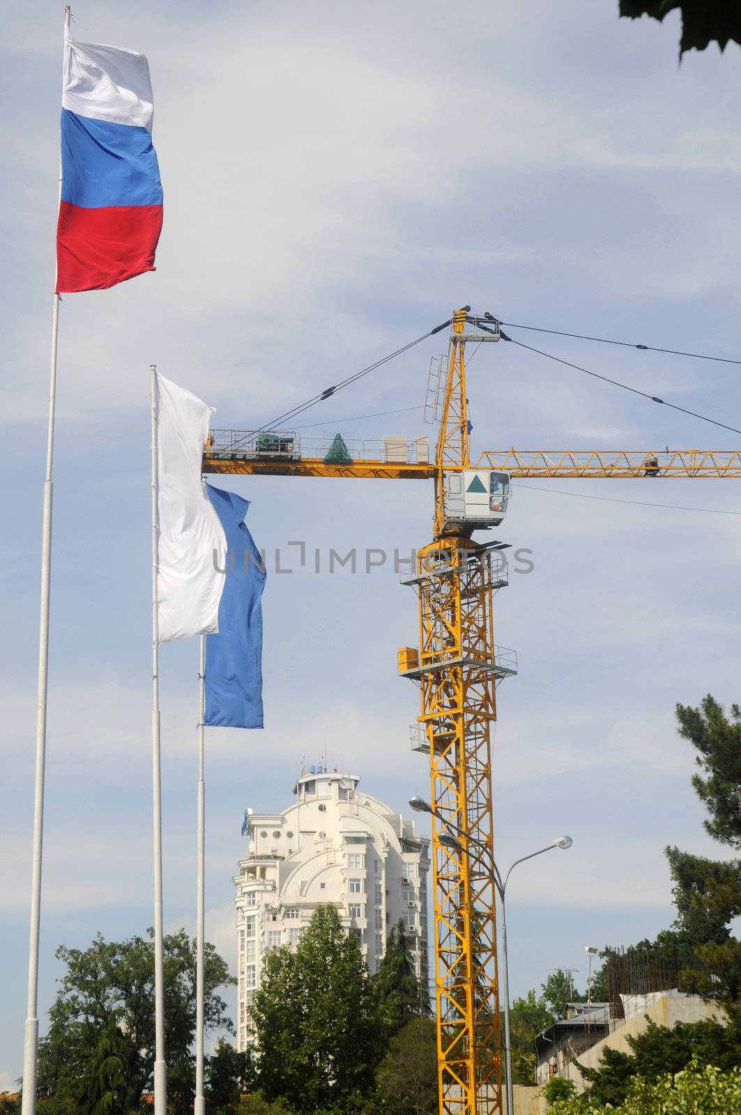 Building crane on sky background and flags of Russia