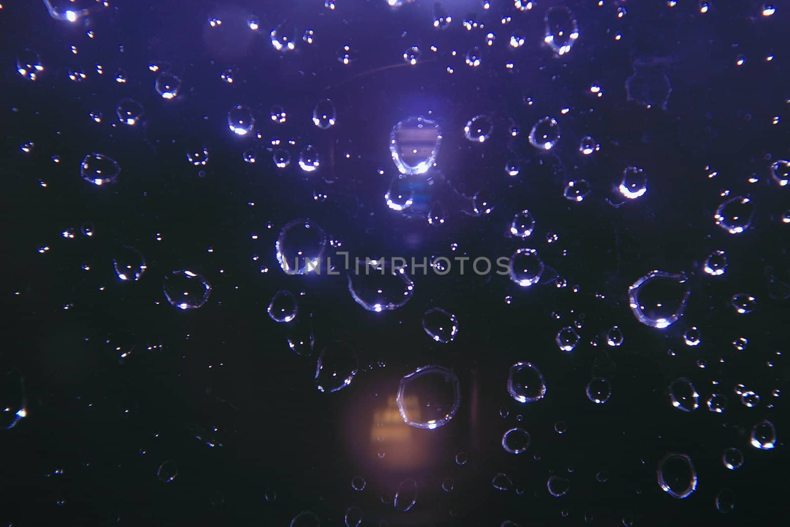 sparkling rain drops on glass against a dark background