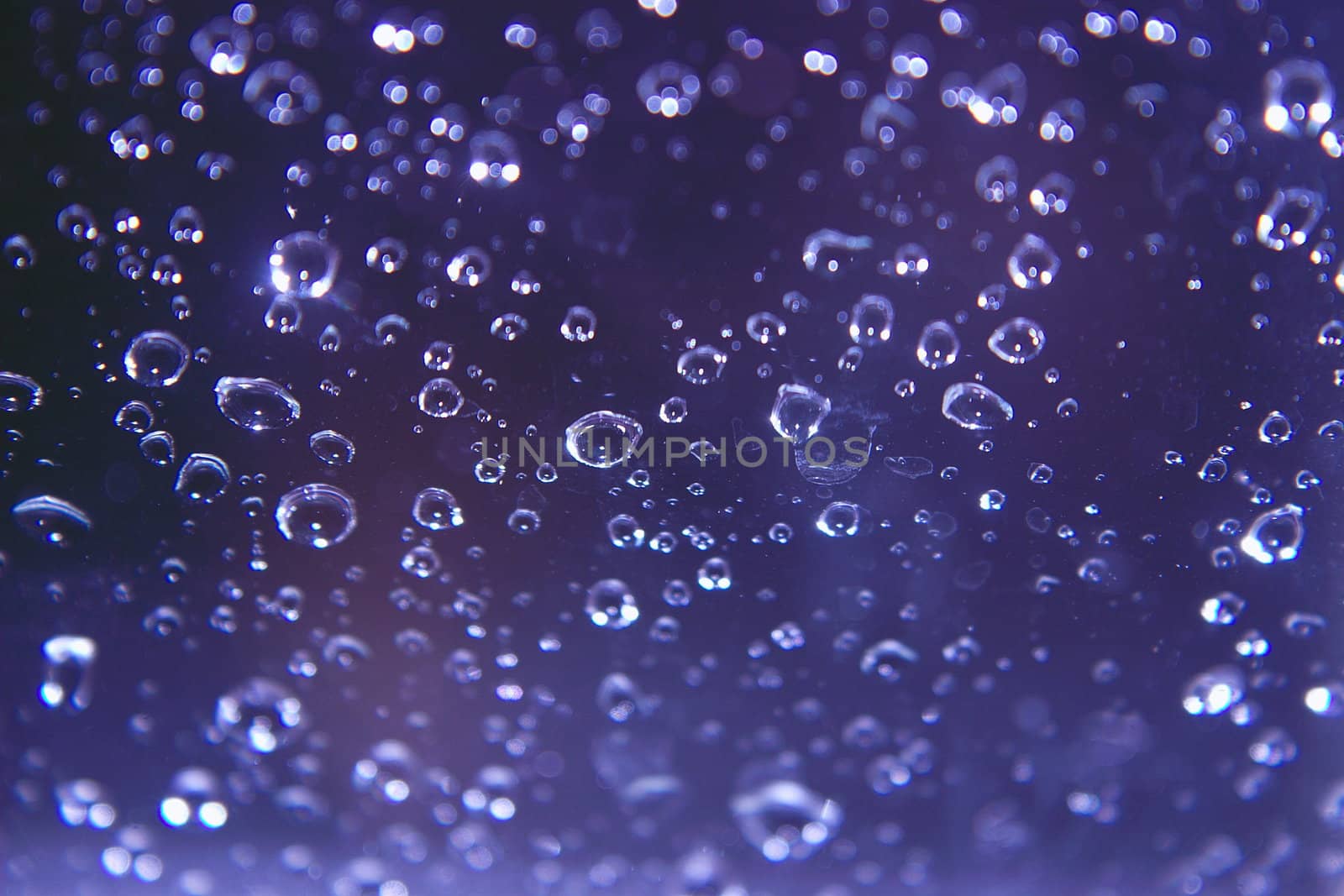 sparkling rain drops on glass against a blue background