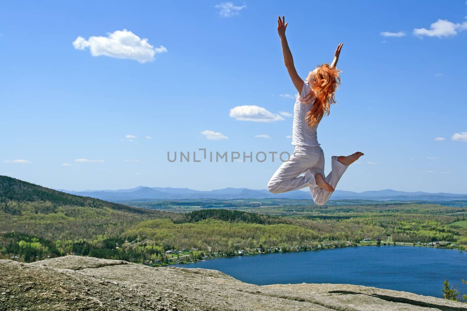 Red-haired girl jumping to the sun on the mountain.
