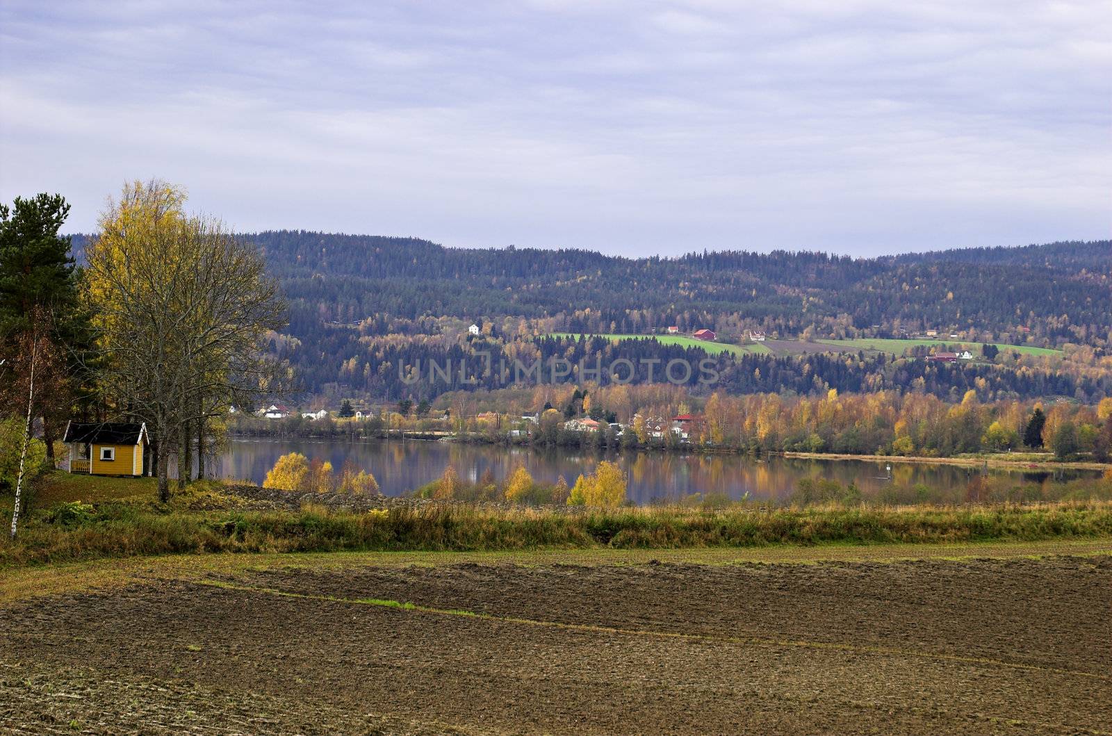 An autumn Norwegian landscaspe. A bare field by the Glomma river, with autumn-coloured hills on the other bank.
