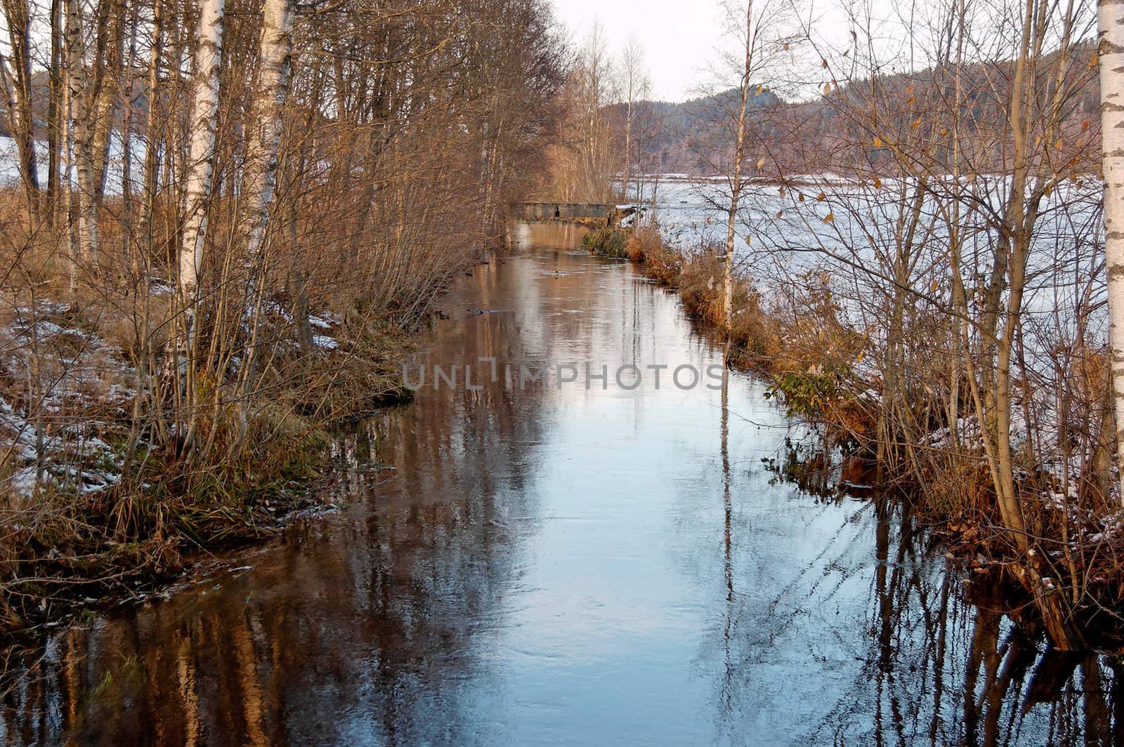 A slow-flowing river in late autumn, with banks covered in snow
