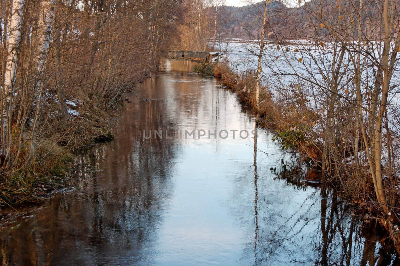 A slow-flowing river in late autumn, with banks covered in snow
