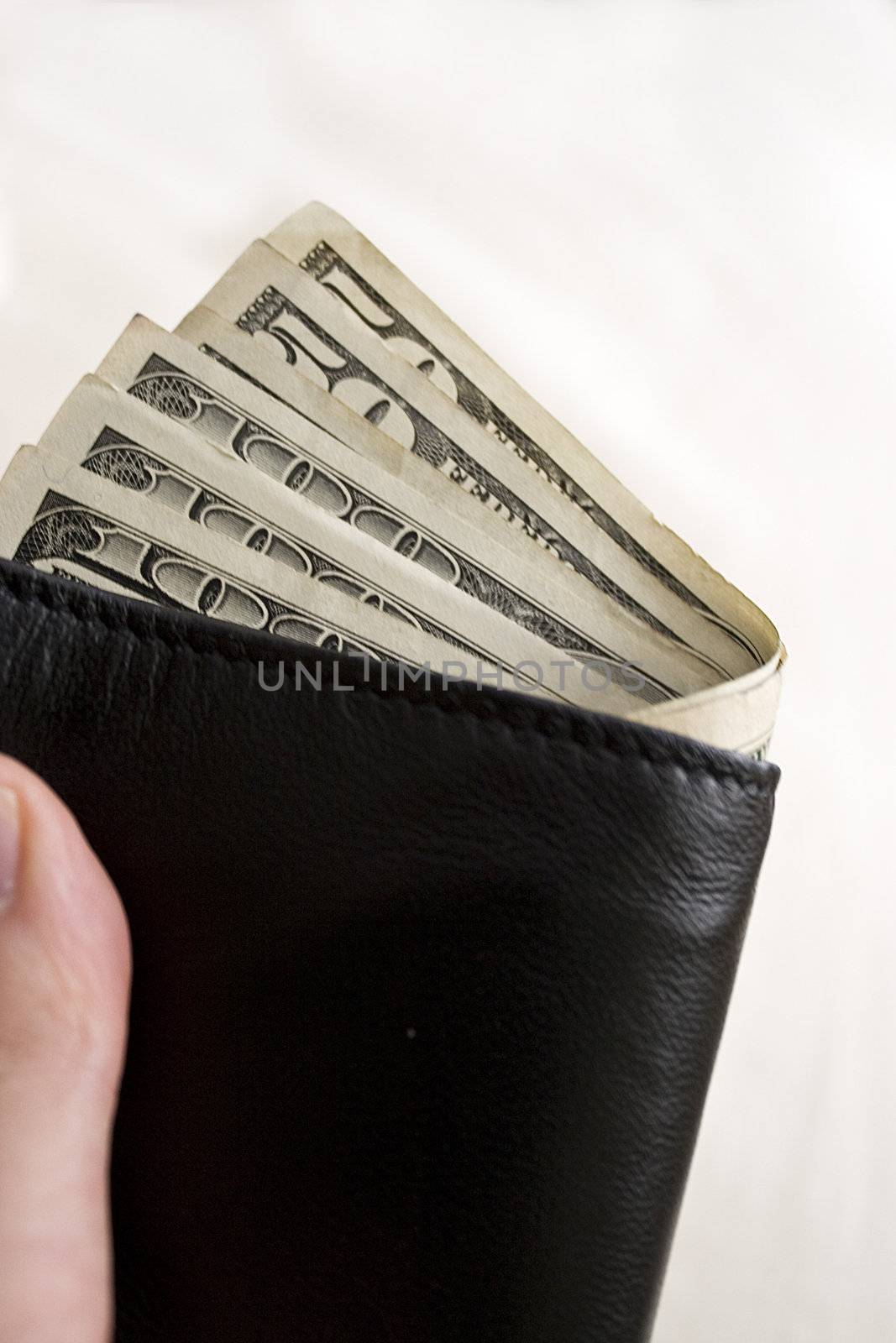 A hand holding a wallet full of cash isolated over a gold background.