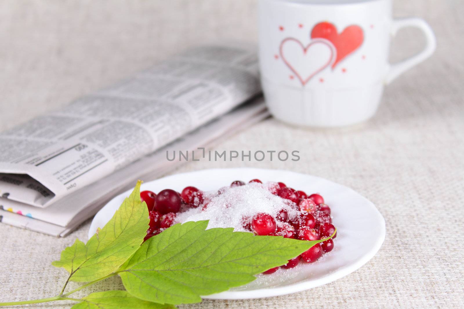 Cowberry in sugar against a mug with hearts and the newspaper removed close up