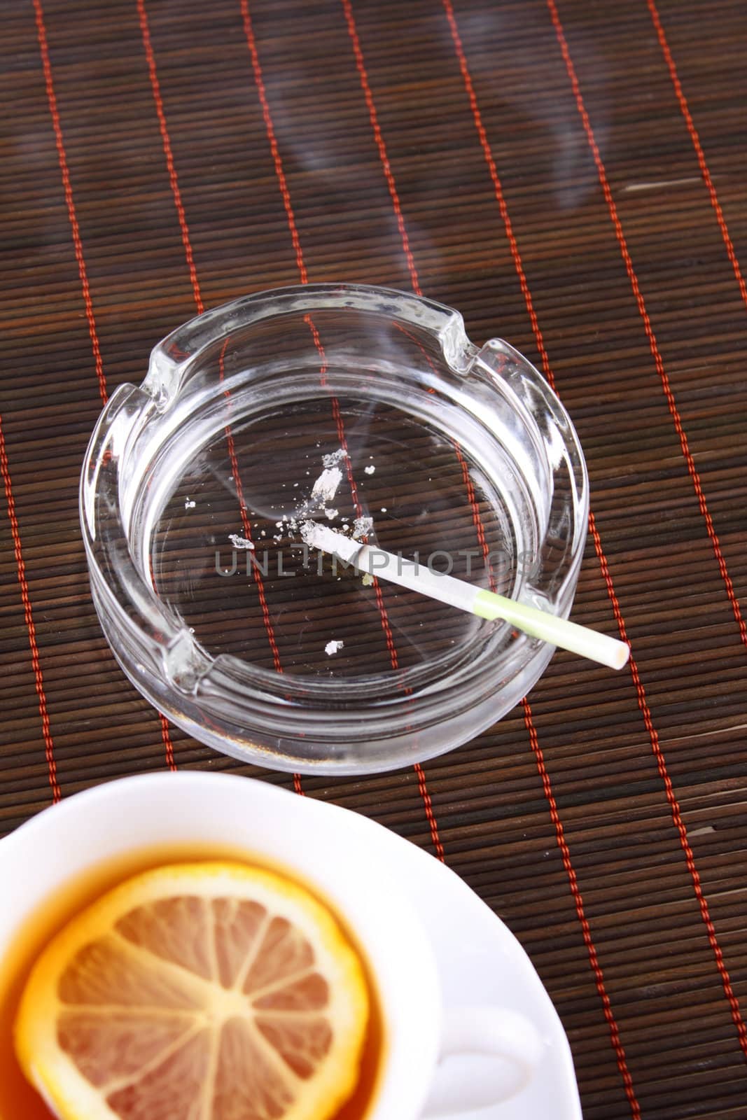 Ashtray with a cigarette and a tea cup on a bamboo napkin removed close up