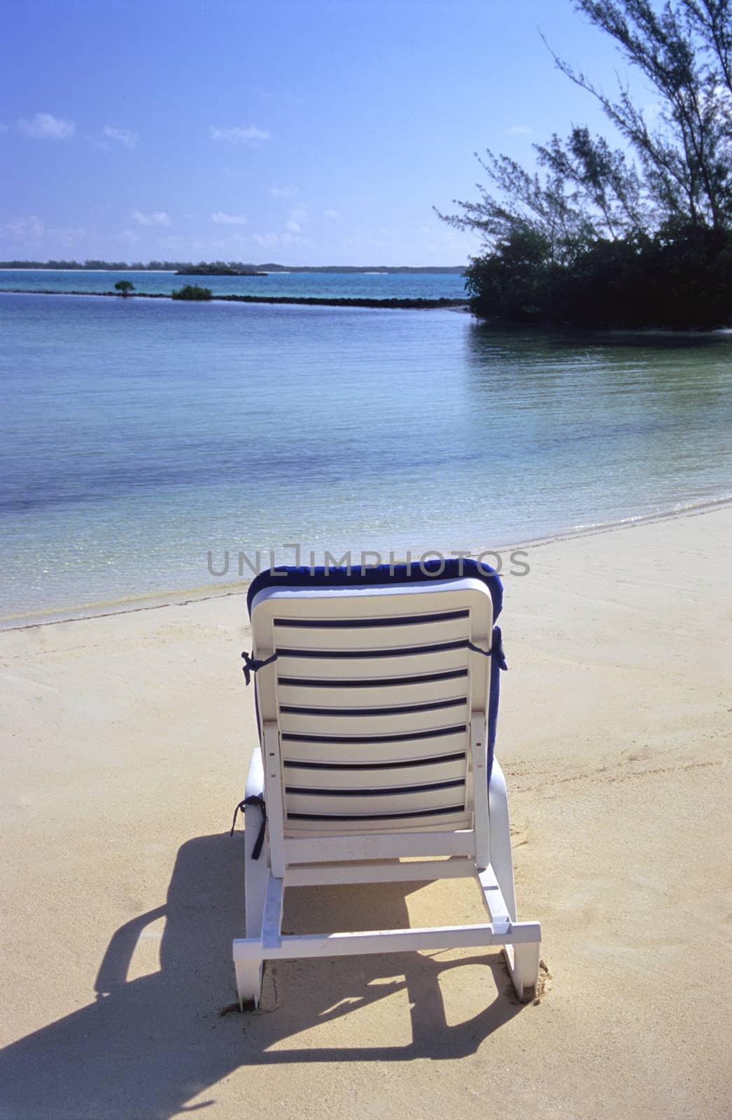 A lounge chair waits for someone to relax in front of the clam waters of the Bahamas.