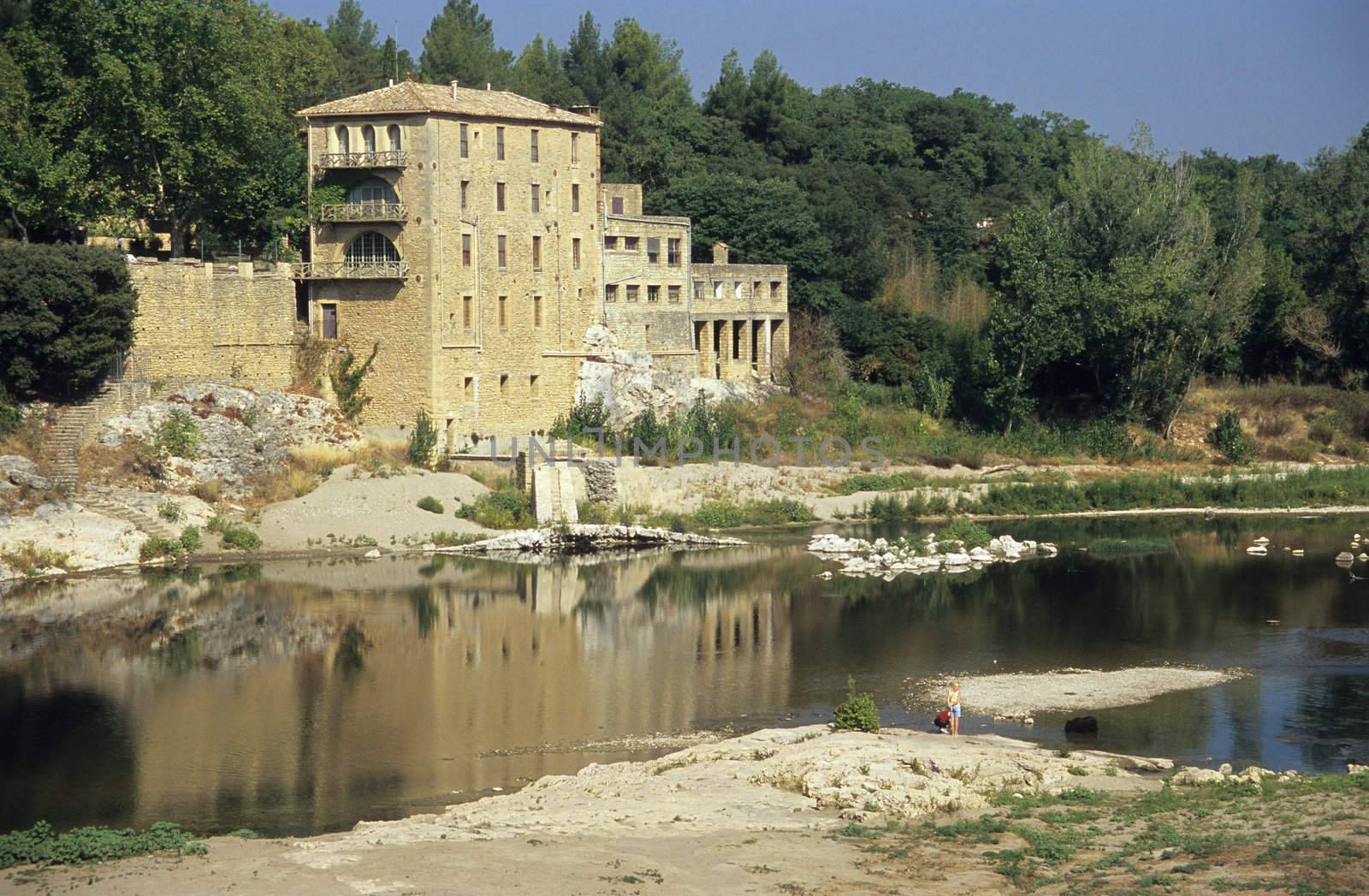 A couple with a dog relax in a river near a stone house, Pont Du Gard, near Nimes, France. 
