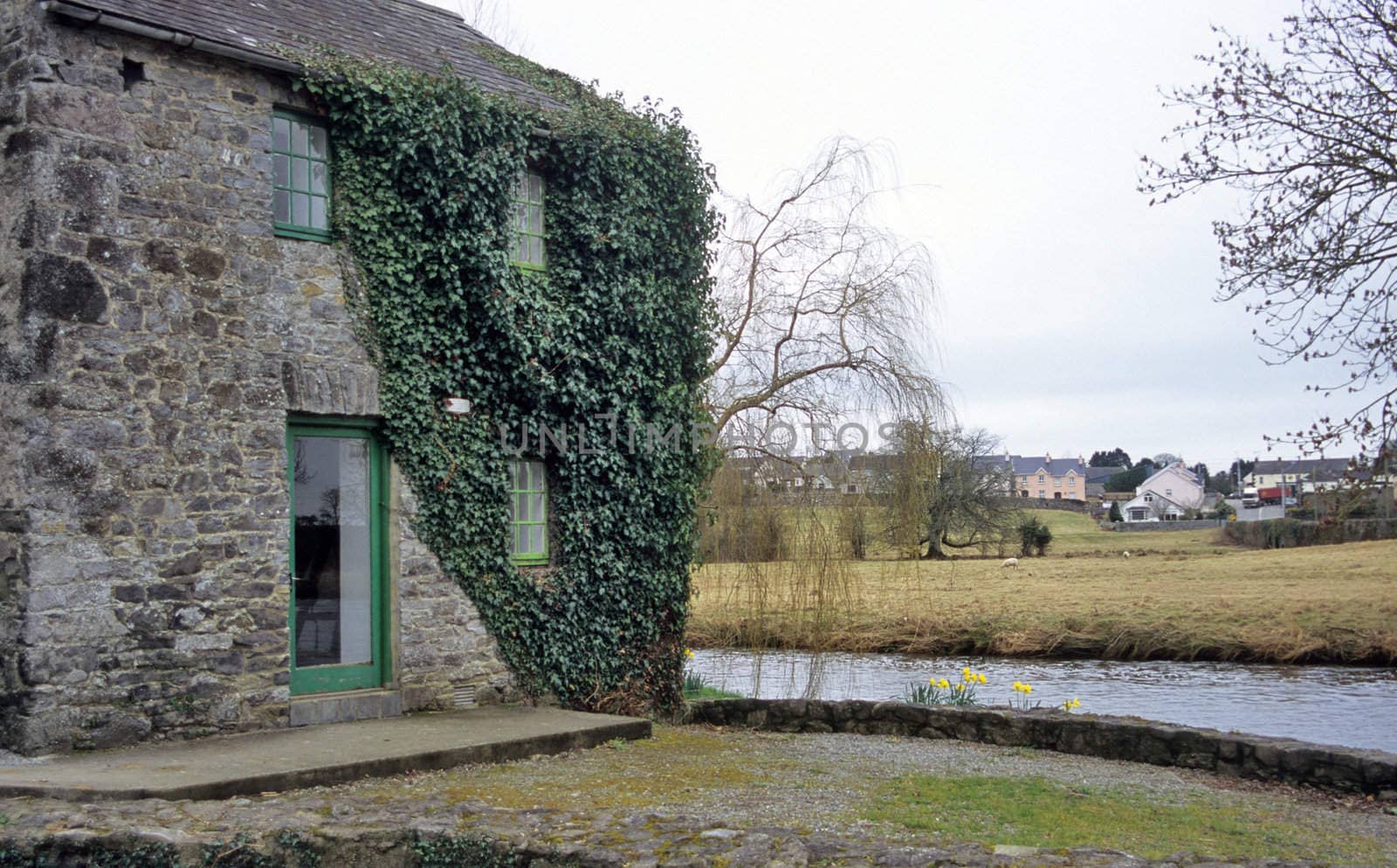An old stone house sits by a river in an Irish village