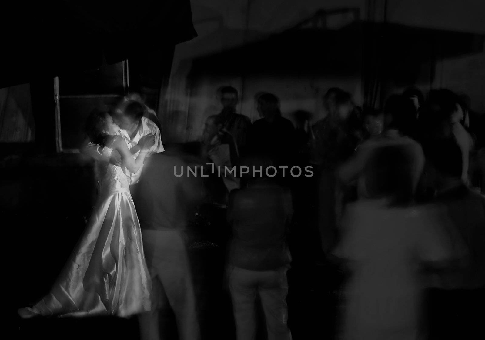 Kissing newlywed in a round of guests. Long exposure shot, focus on bridge, peoples blurred. Black and White shot