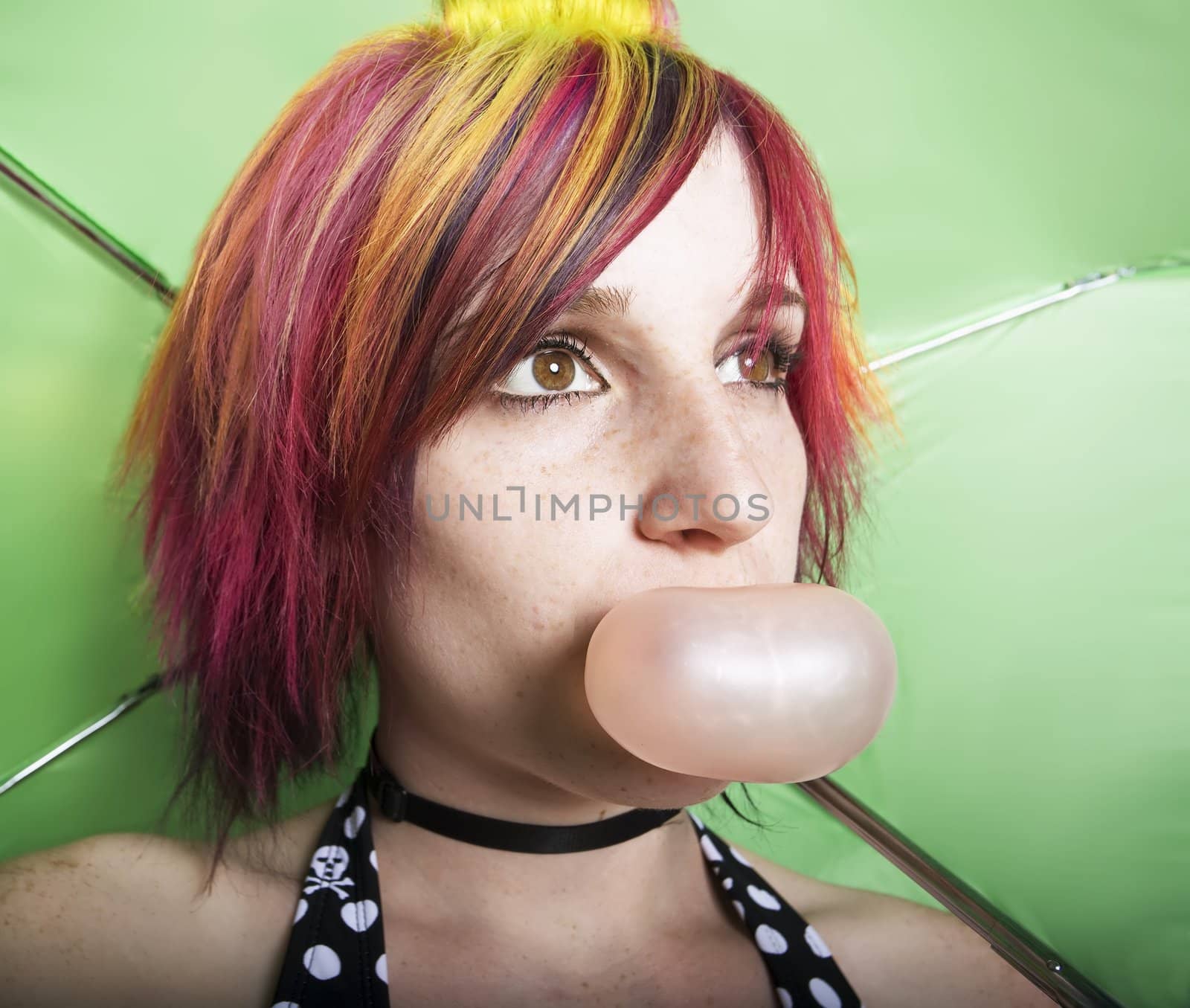 Closeup woman in front of a green umbrella blowing a bubble