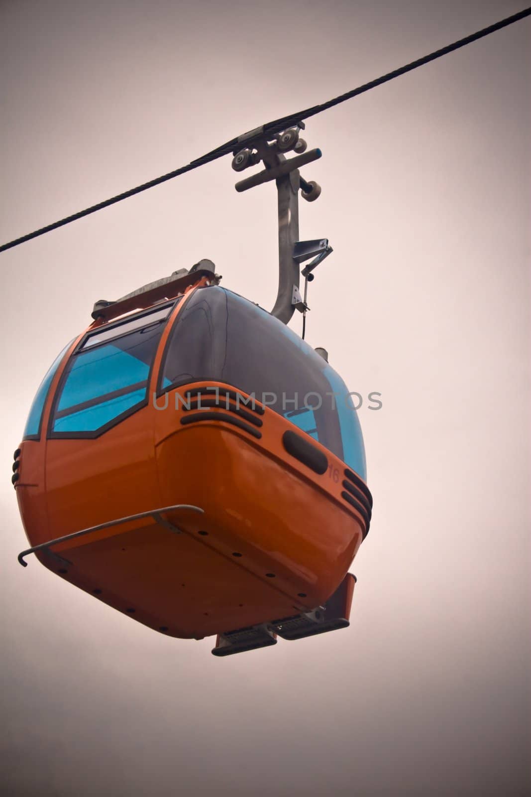 New orange mountain gondola suspended from wire against white sky with vignette