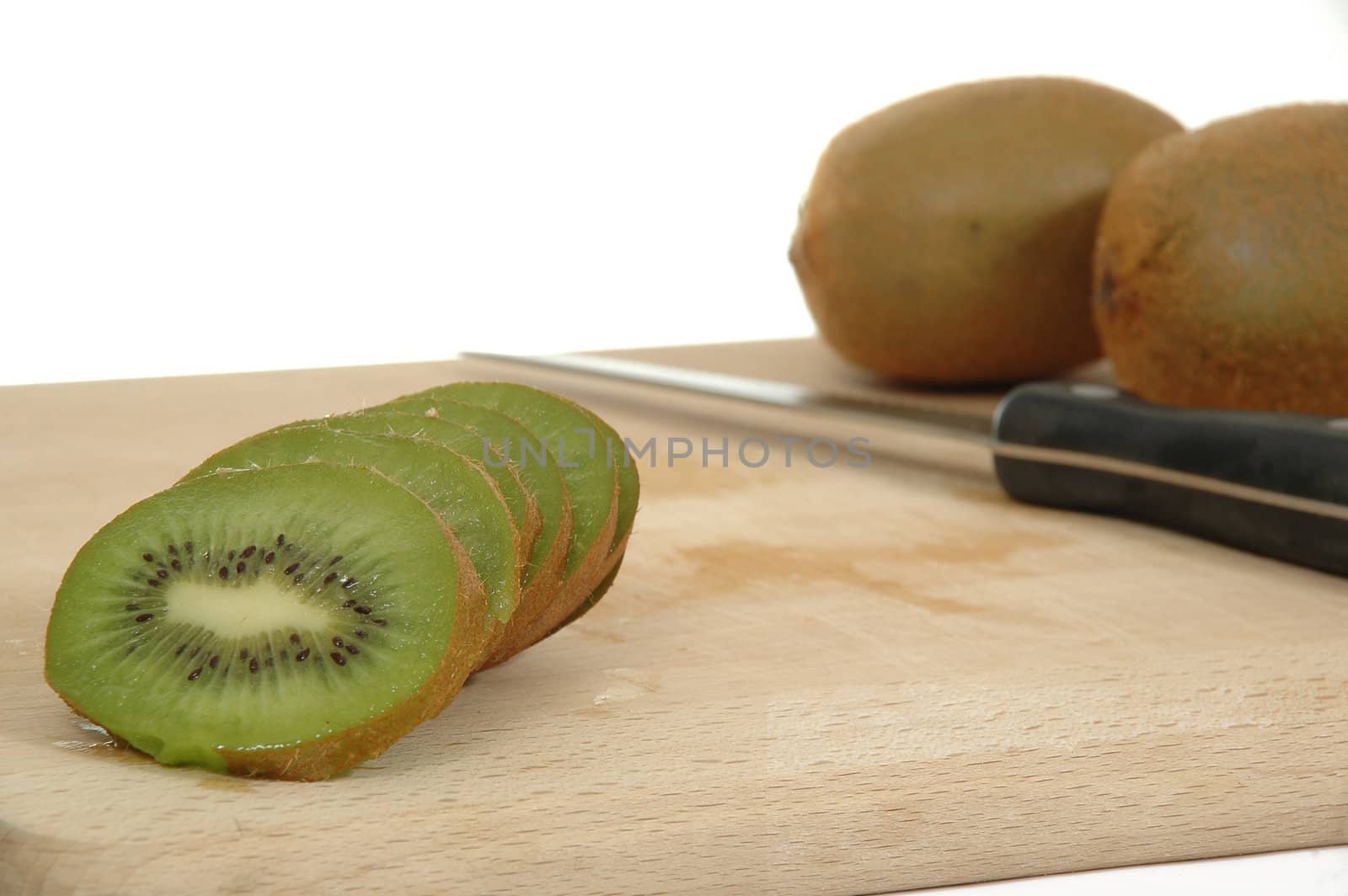 Kiwi slices is in focus. With knife and kiwies in the background.