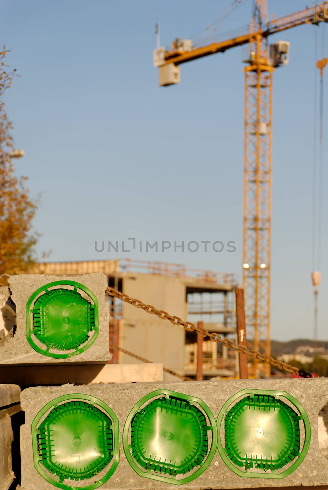 Concreted block at a construction site, plugged with green, with crane at the background
