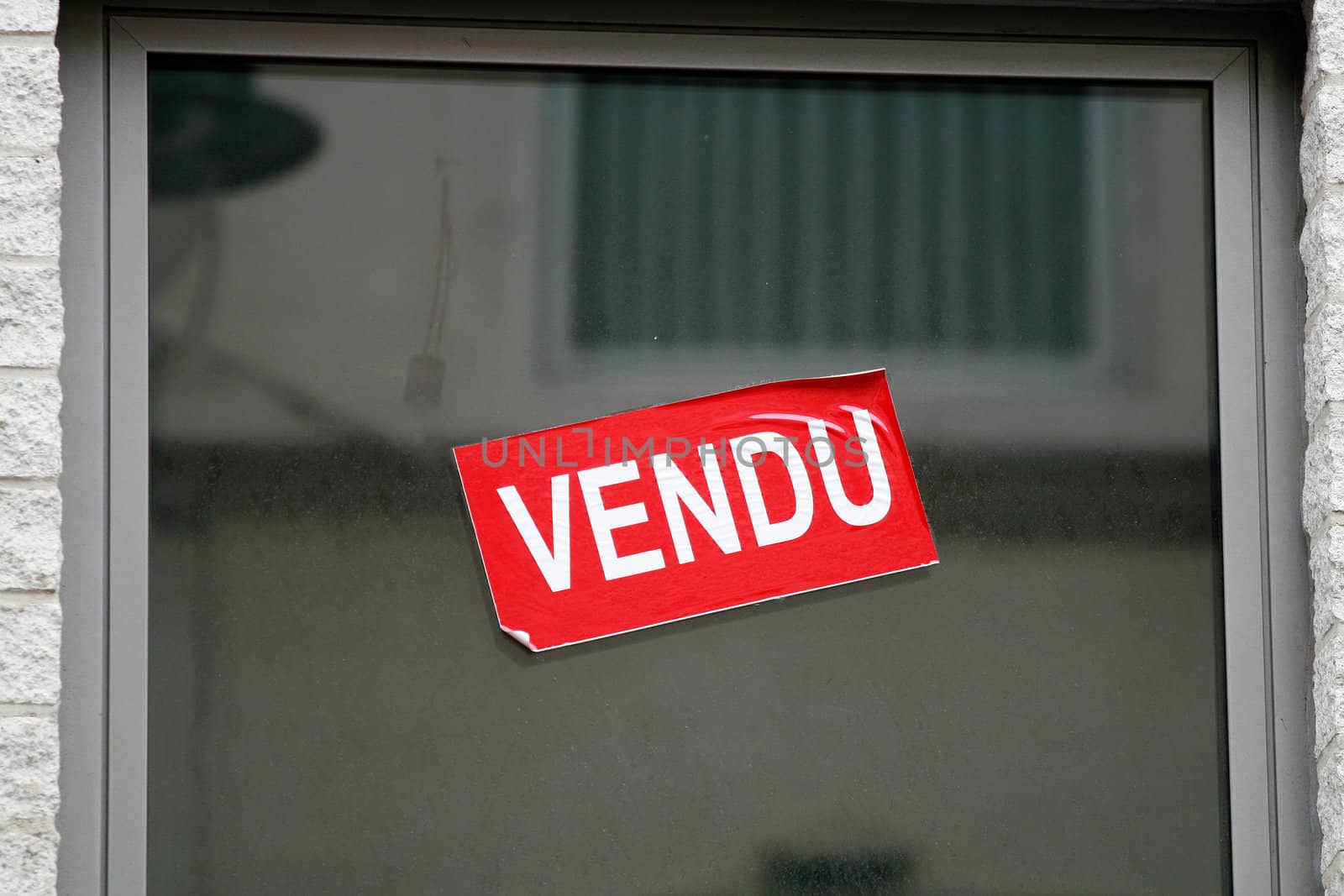 Window with Red and white sticker with word Vendu that means Sold in french