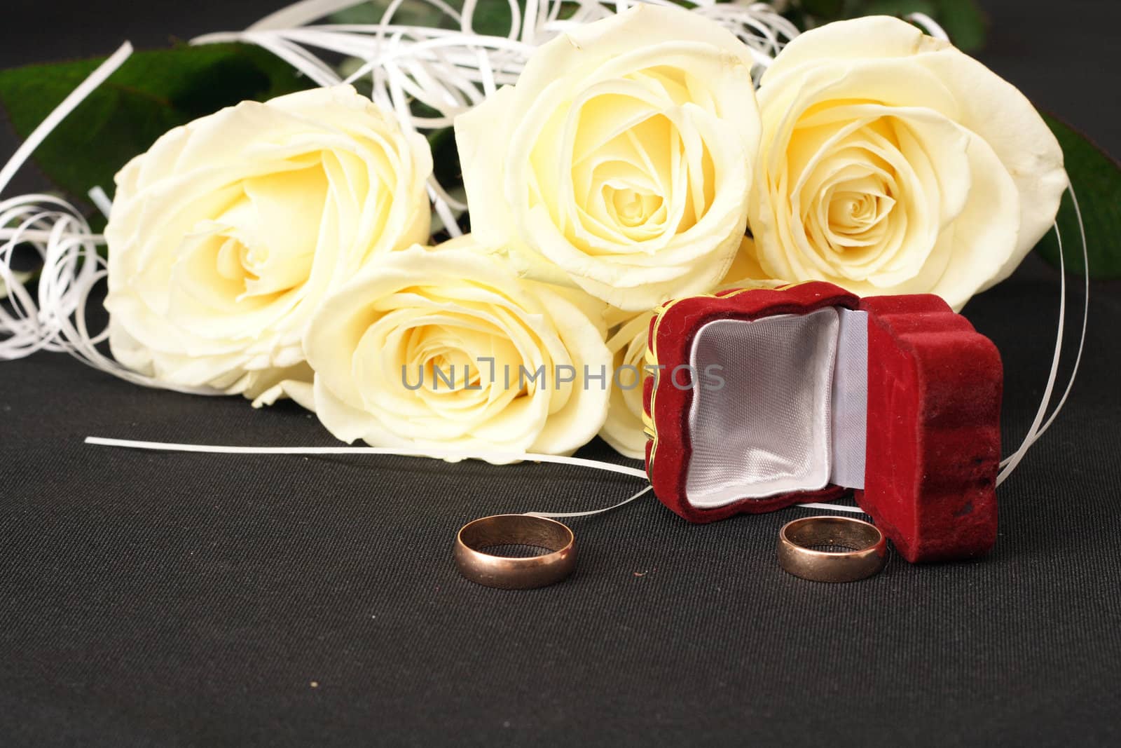 wedding rings box and white roses on black background