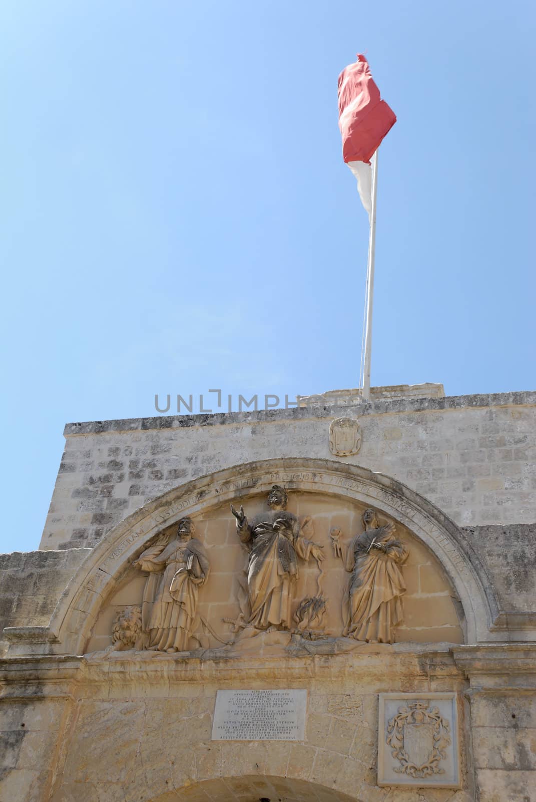 The entrance gate to Mdina on Malta, with Maltese flag St. Peter sculpture group. The writing is in Latin from the 14th century.
