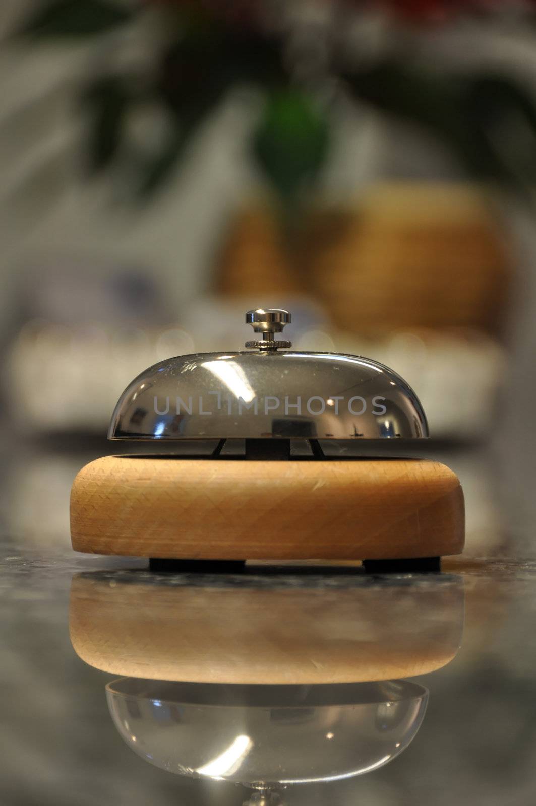 Detail shot of a service bell located on a hotel reception desk with blurred details in the background and reflection on marble counter