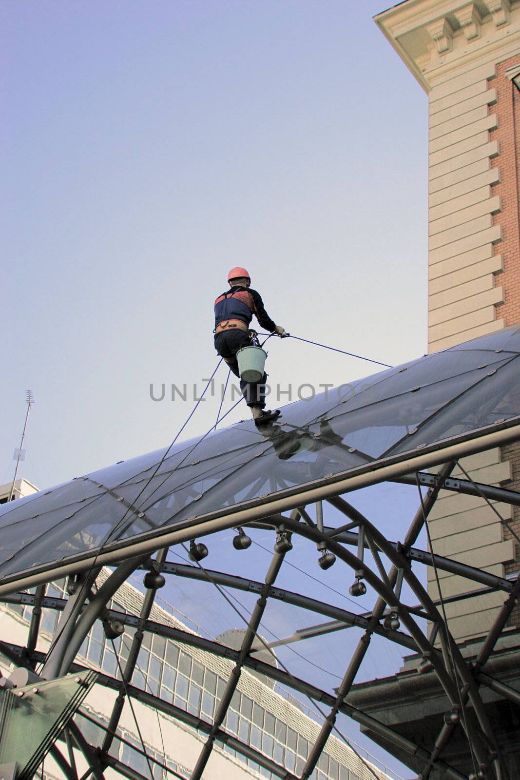 One worker cleaning glass on  building's roof. 