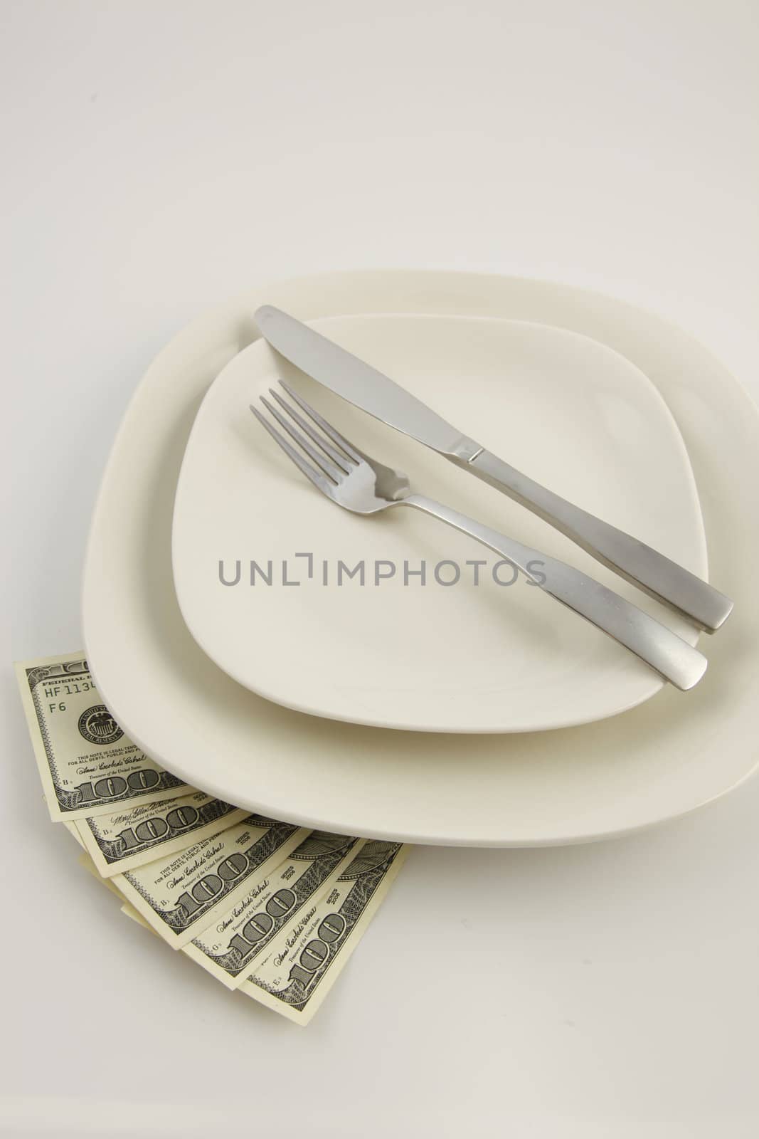 Five 100 US Dolllar bills under a white plate with a knife and fork
