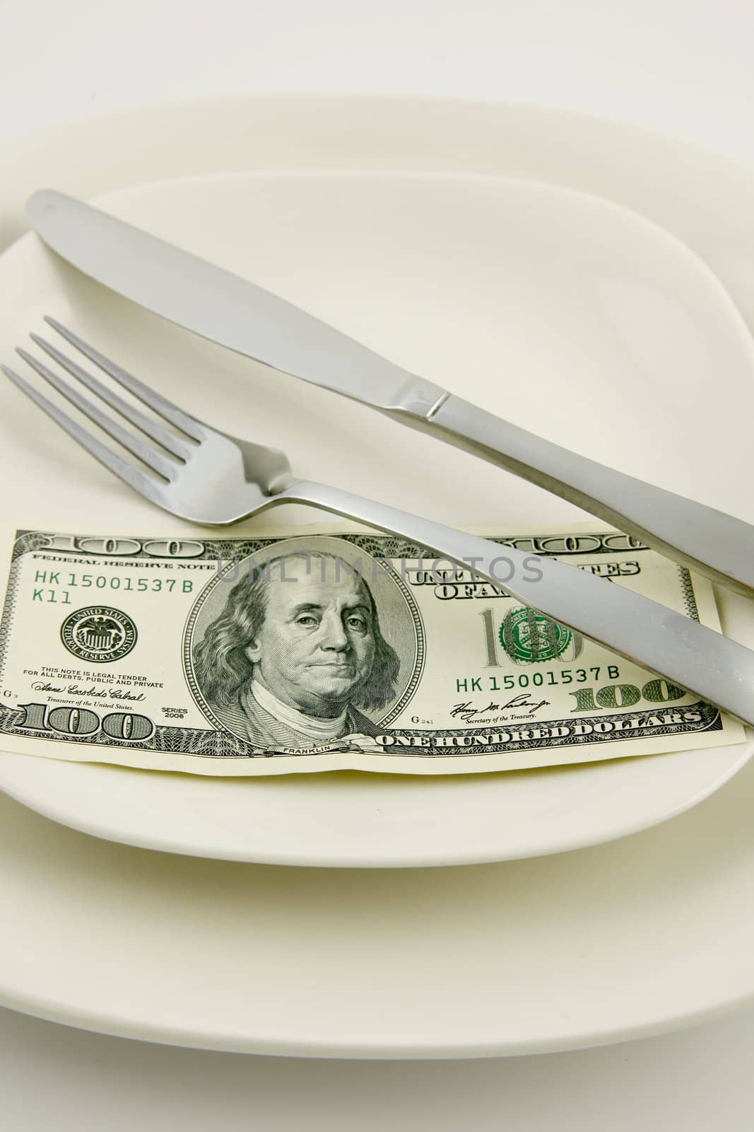 A one hundered United States dollar on a plate with a knife and fork