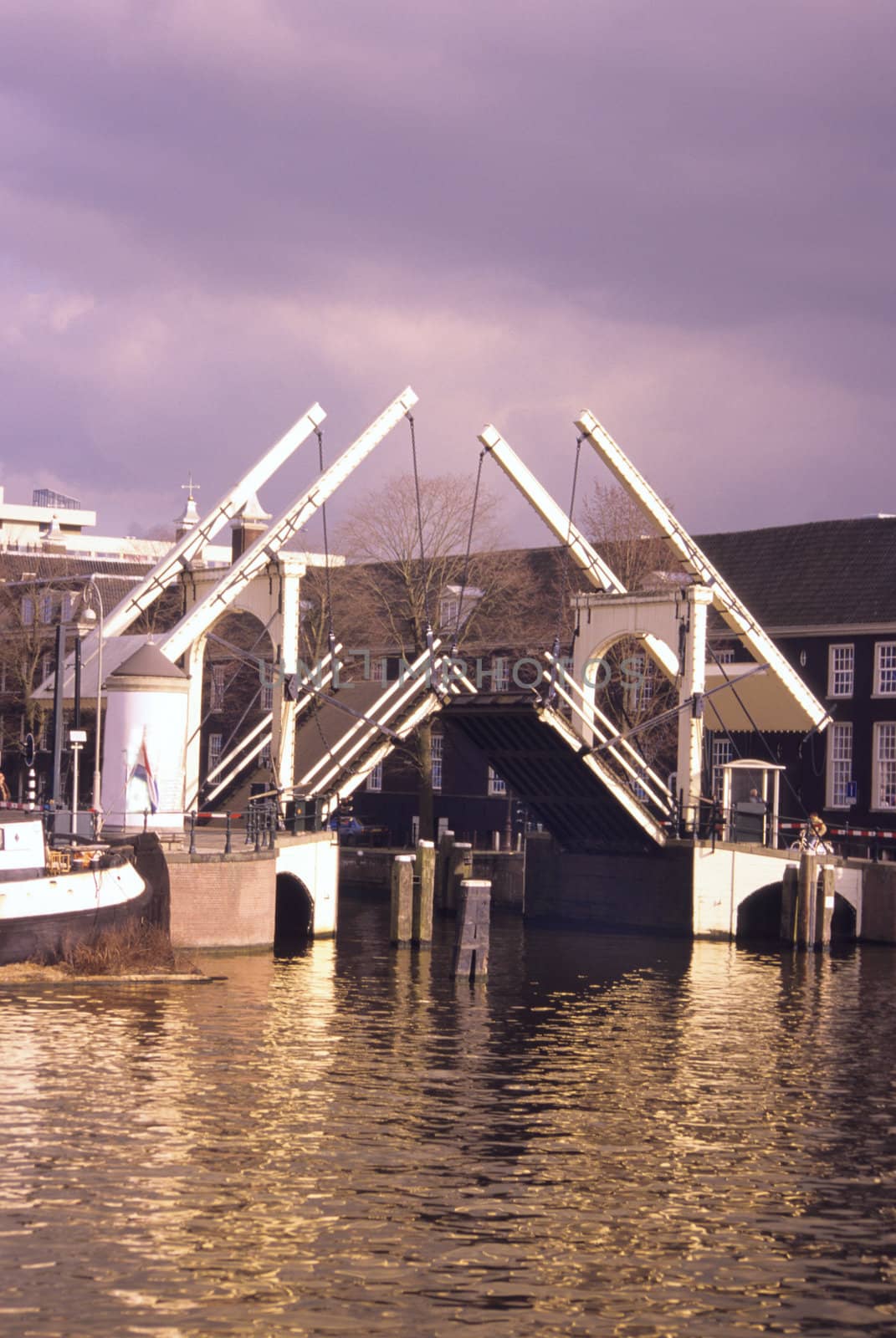 A traditional dutch drawbridge opens over a canal at sunset