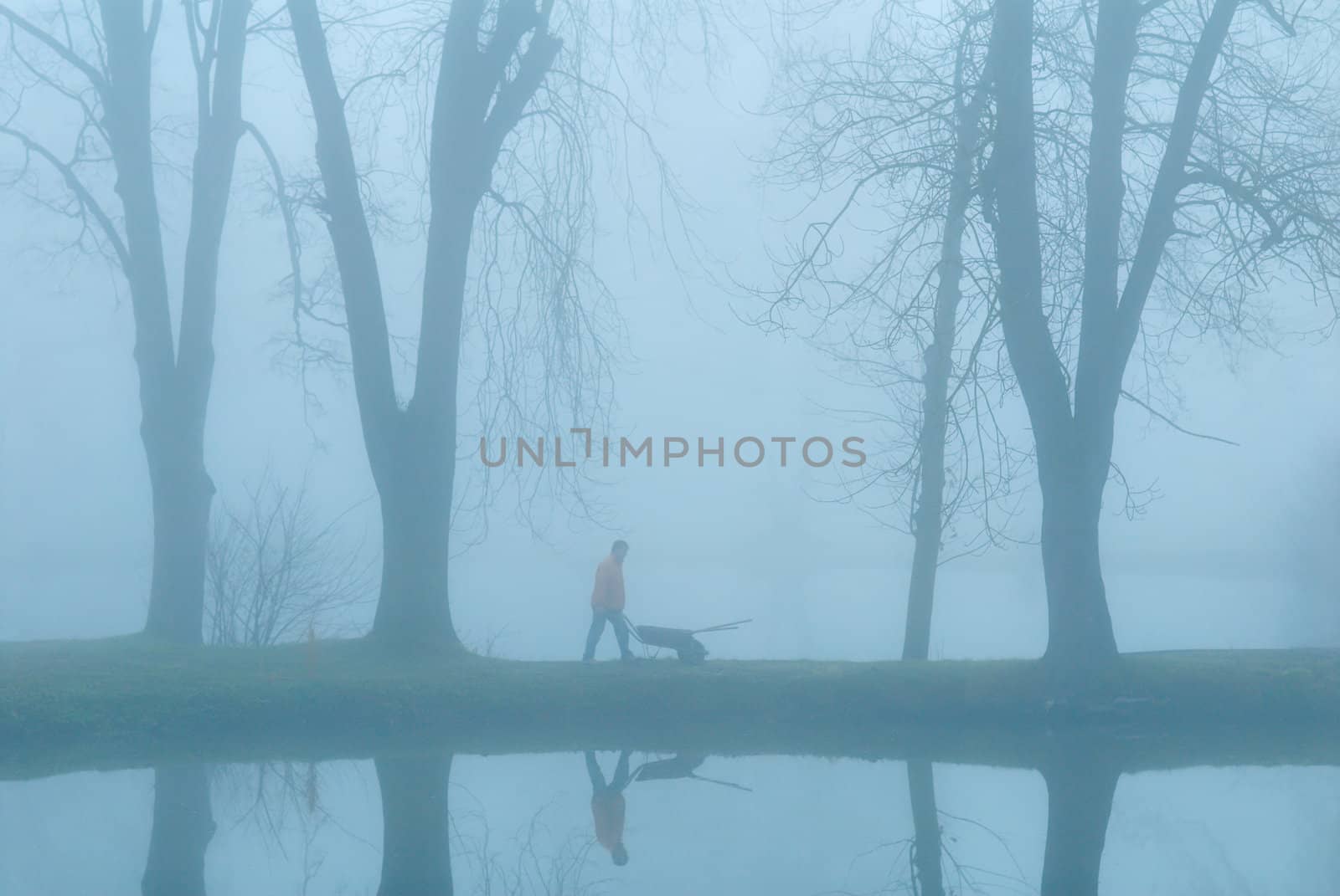 The gardener on coast of lake. Earlier morning. A fog