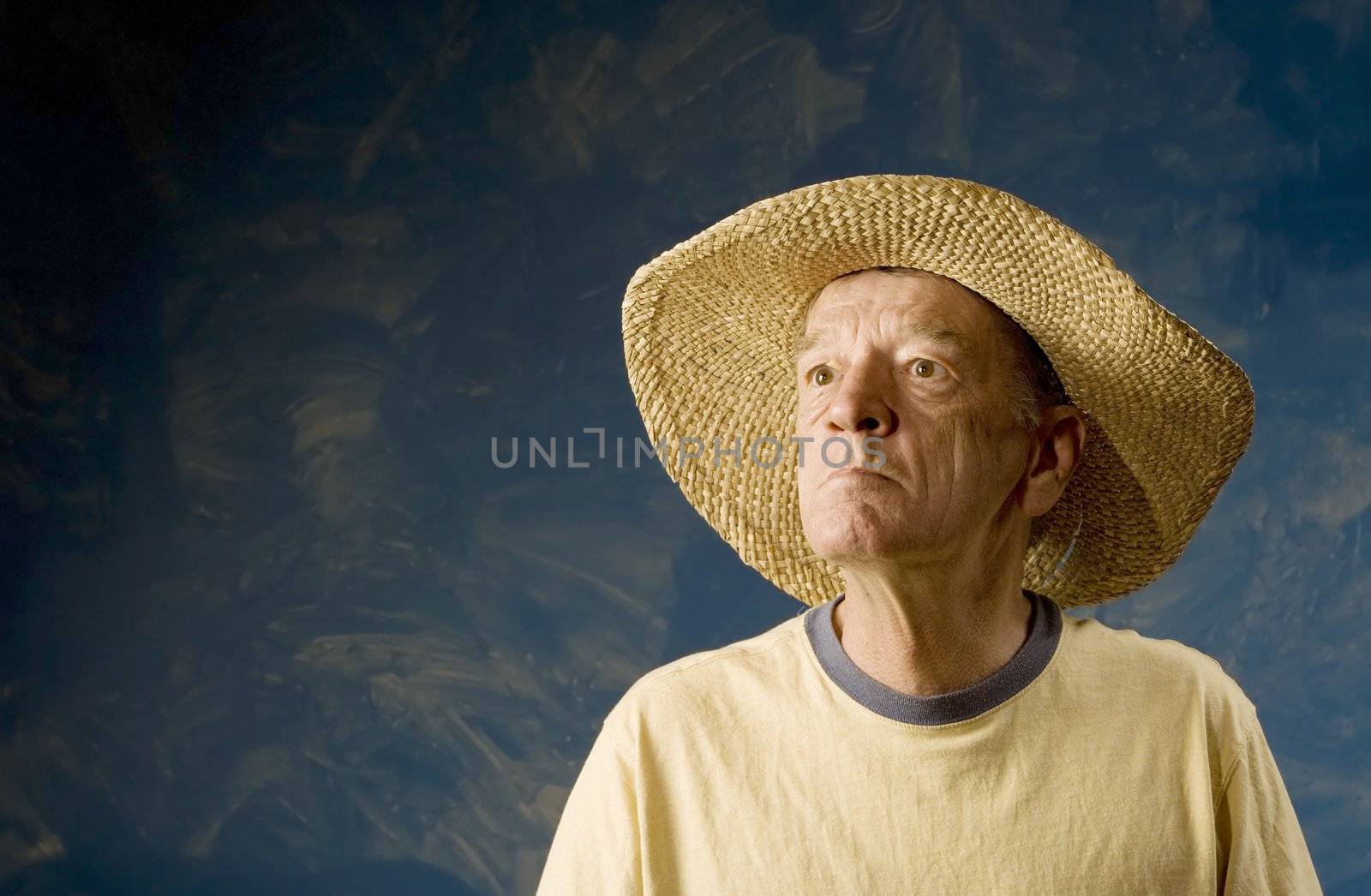 Senior man in a straw hat in front of blue set wall