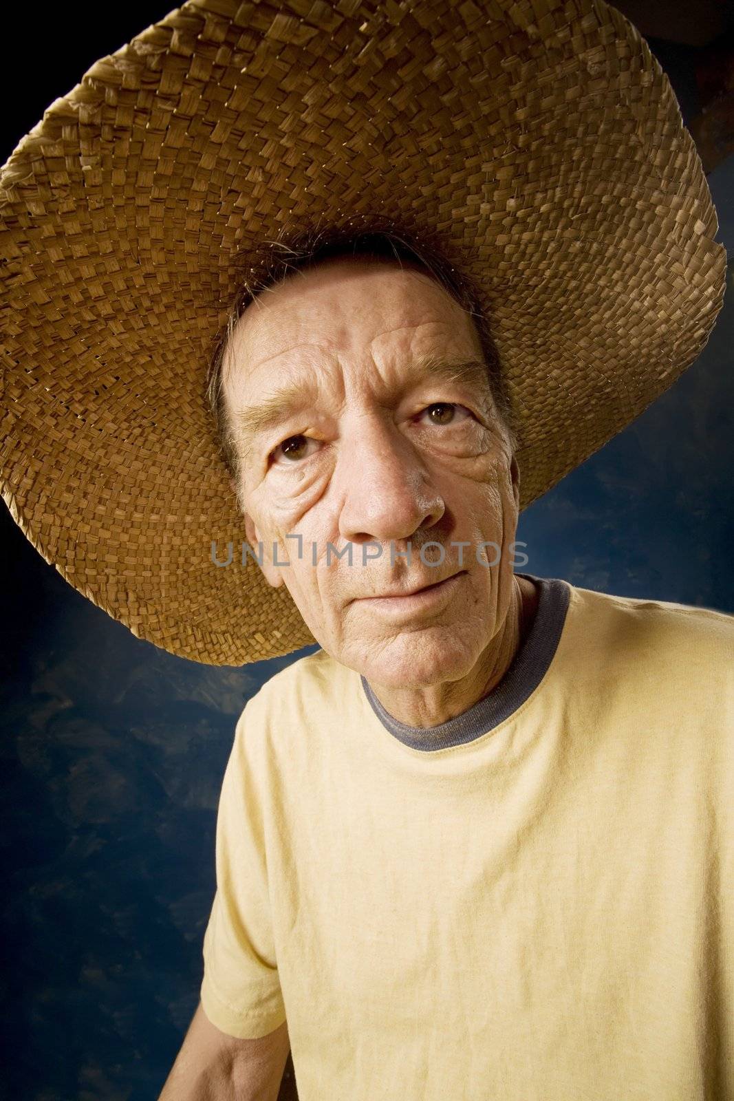 Senior man in a  big straw hat in front of blue set wall
