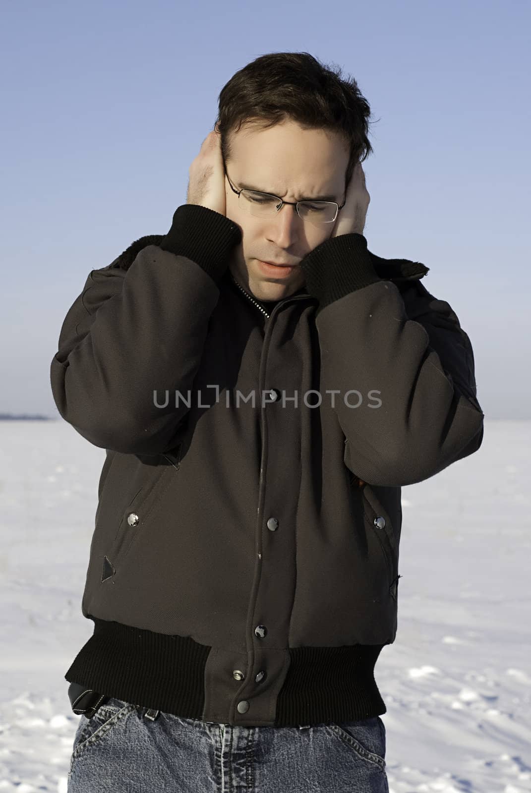 A young man standing outside in the winter, holding his ears to keep them warm