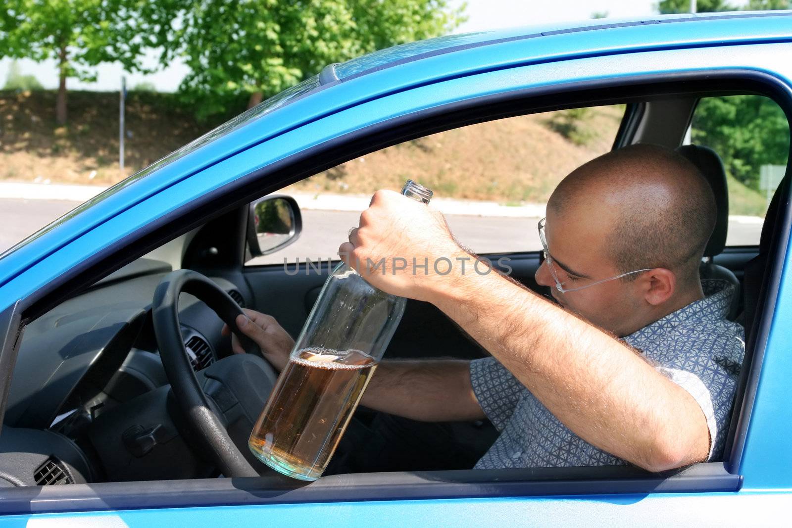 Drunk man sitting in drivers and holding a bottle alcohol