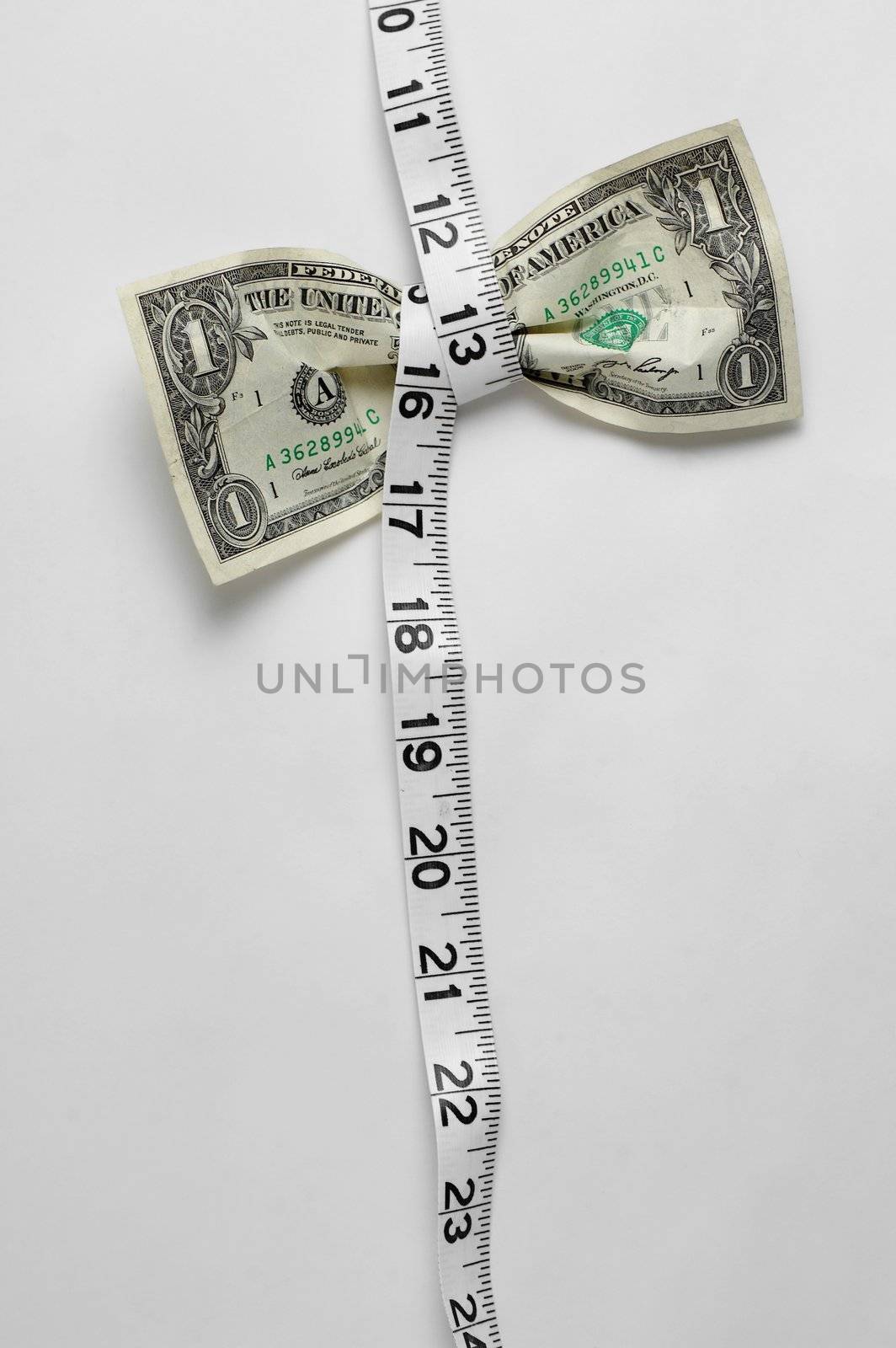 Dollar bill being squeezed by tape measure on white background.