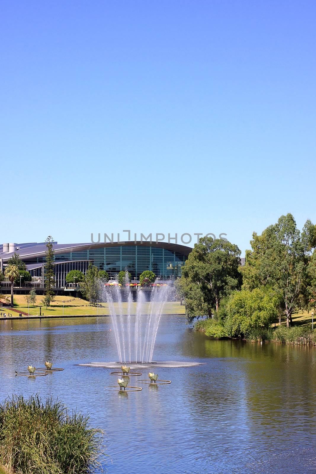 Adelaide Convention Centre along the banks of the River Torrens Lake, with a water fountain and 'paper boats' sculpture in the foreground.  Adelaide, Australia