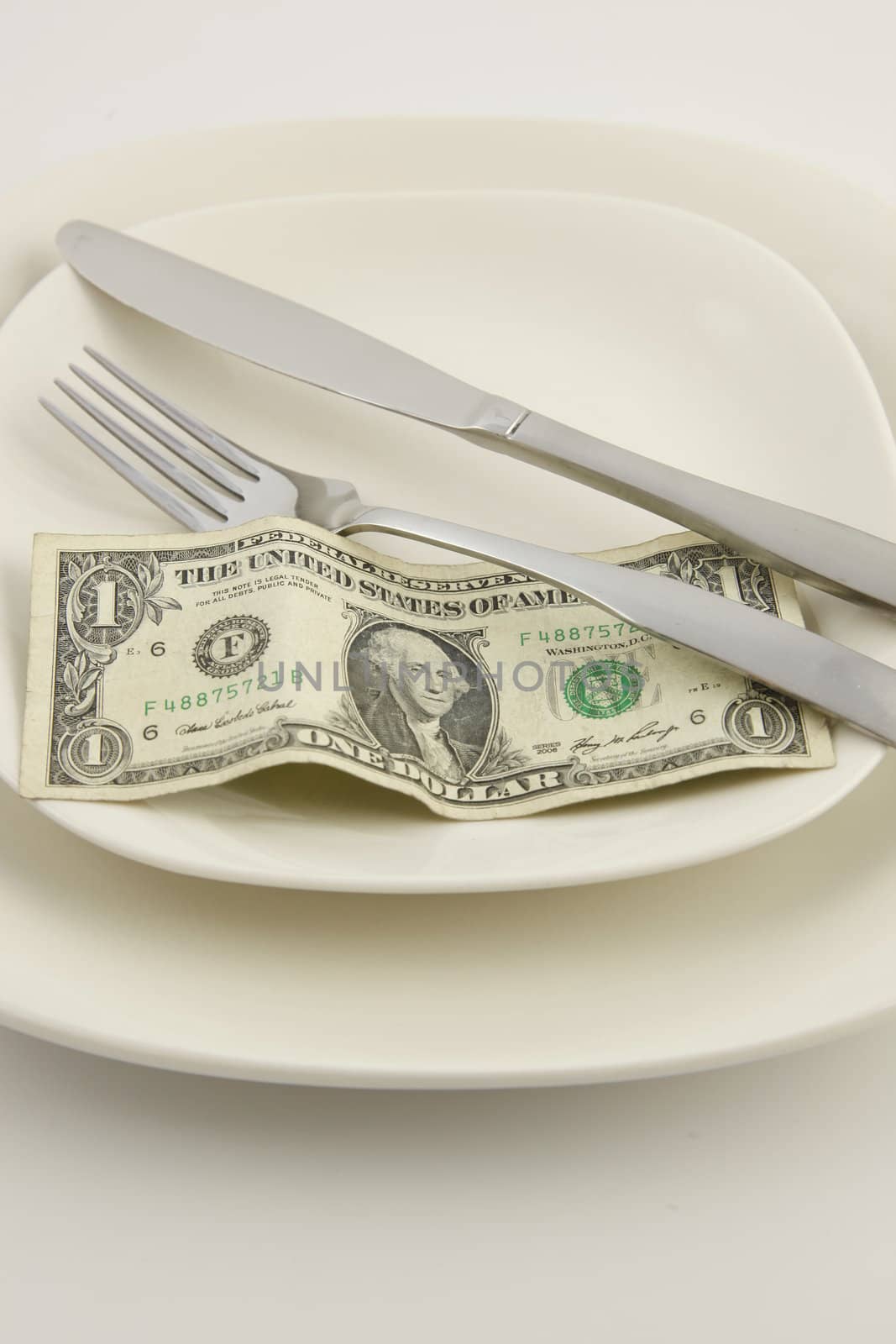 A United States one dollar bill on a white plate with a knife and fork