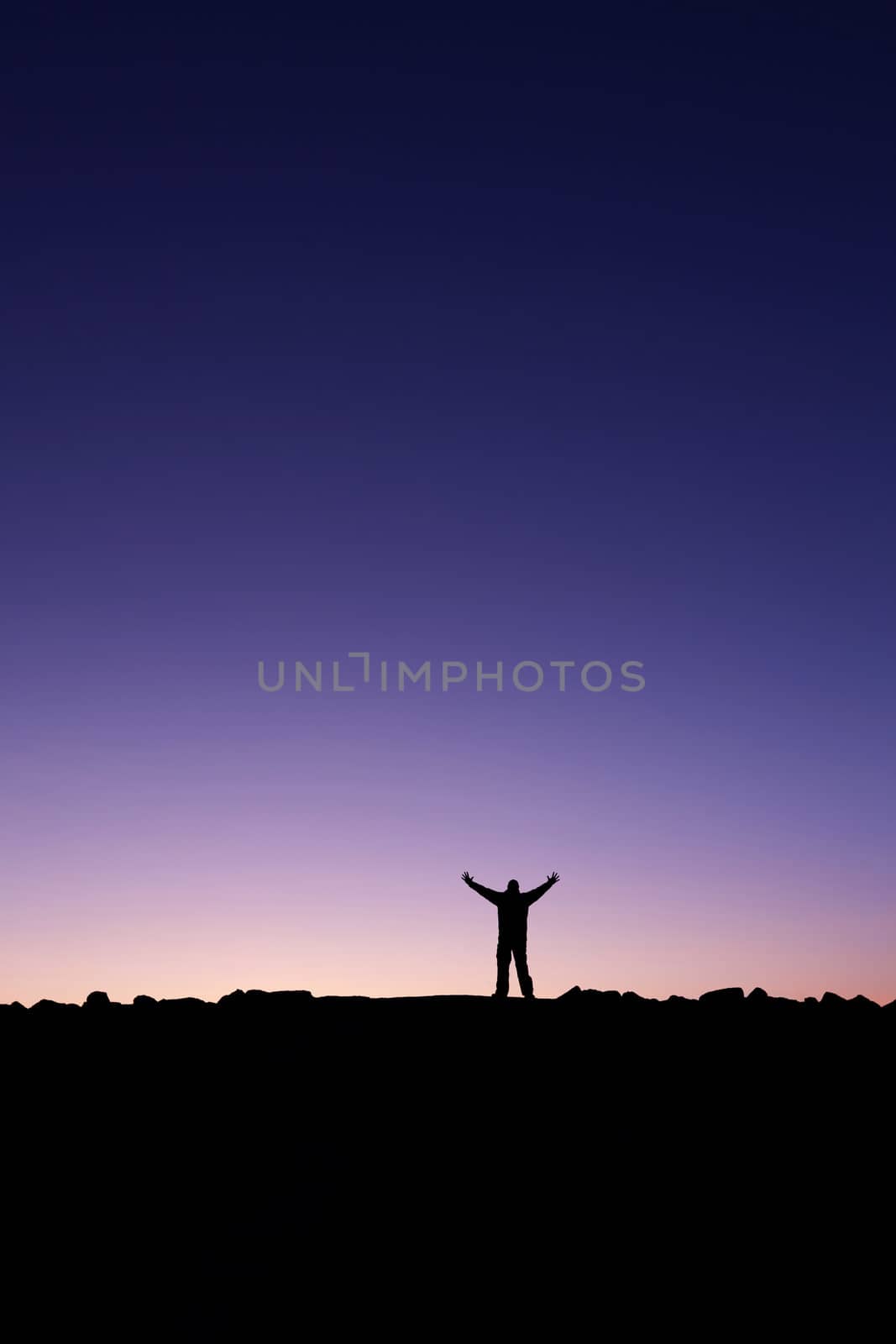 Silhouette of a man raising his hands into the sunrise after conquering a summit