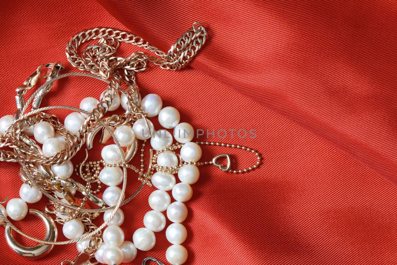 Pearl necklace and gold jewelry lying on red silk background with copy space