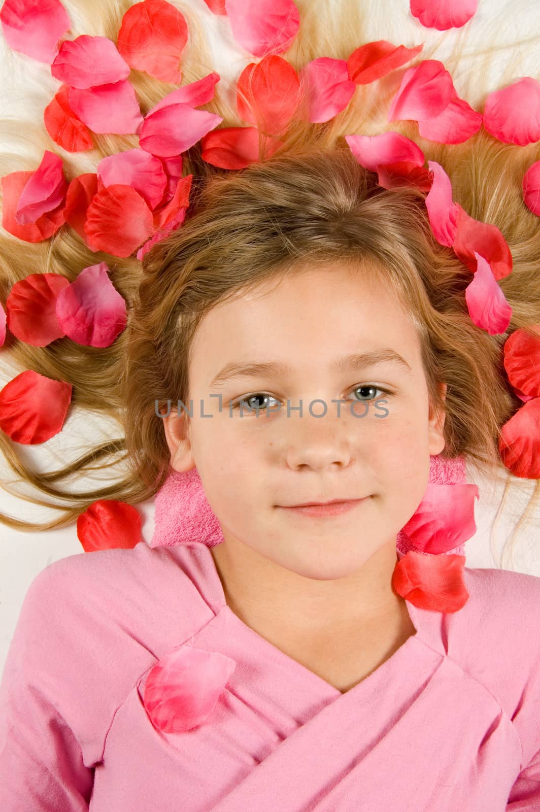 Beautiful girl lying in rose petals on white