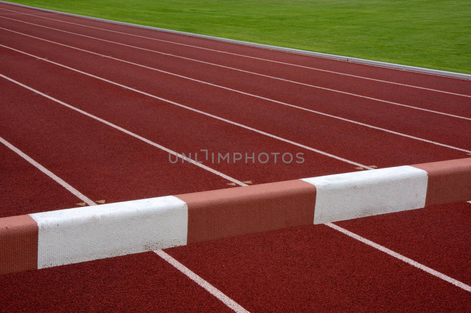 steeplechase barrier across red running tracks with white lines and green field in a background