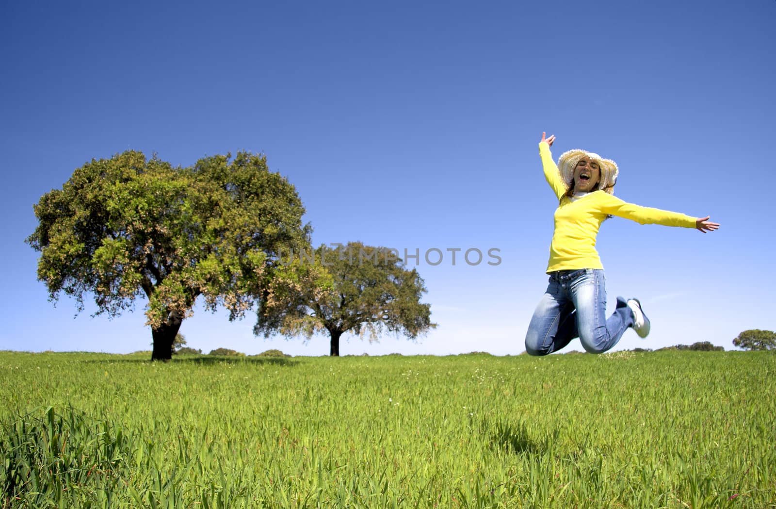 Haapy woman jumping on a beautiful green meadow with trees