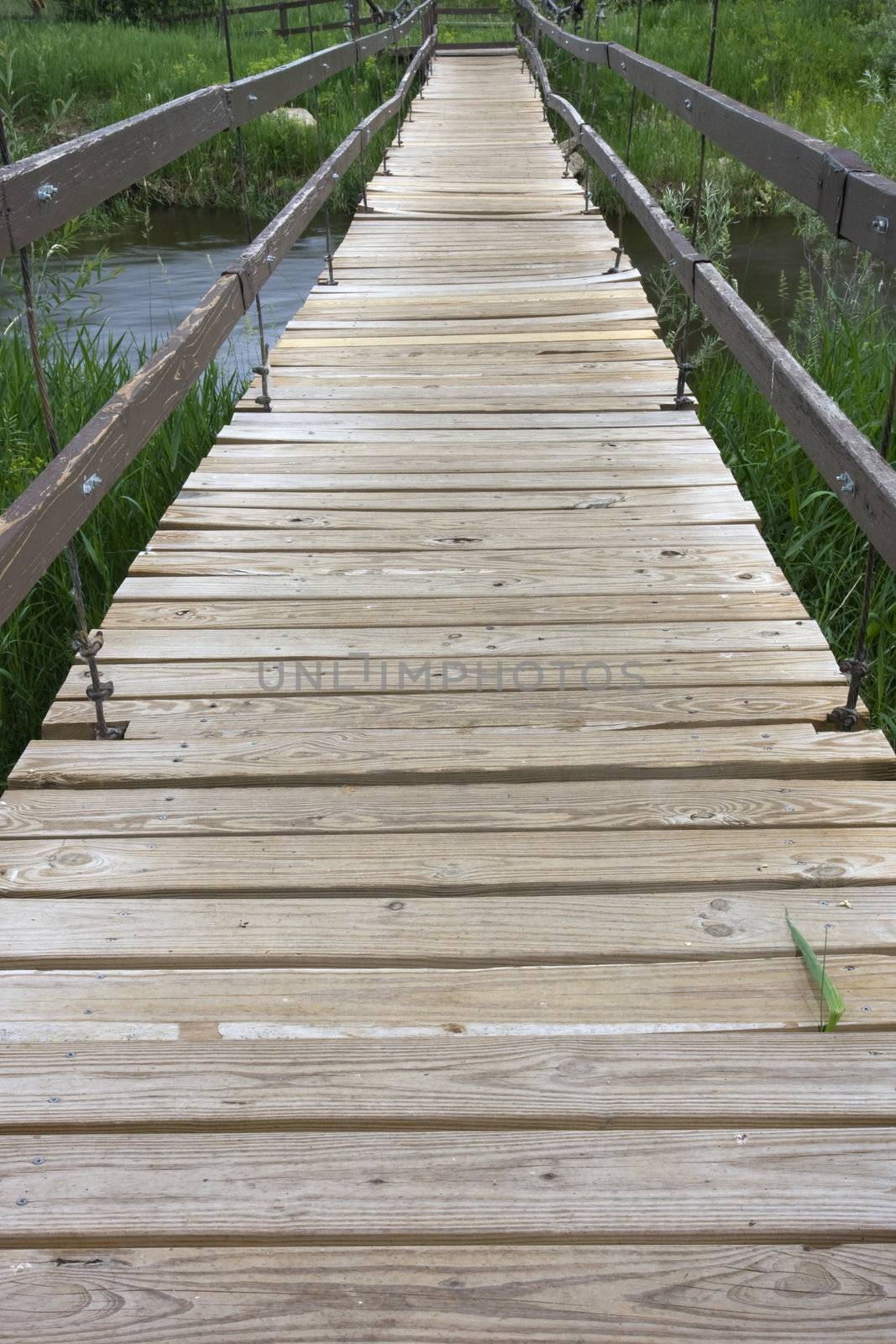 suspended footbridge over a small river, emphaisis on pathway with wooden rough planks