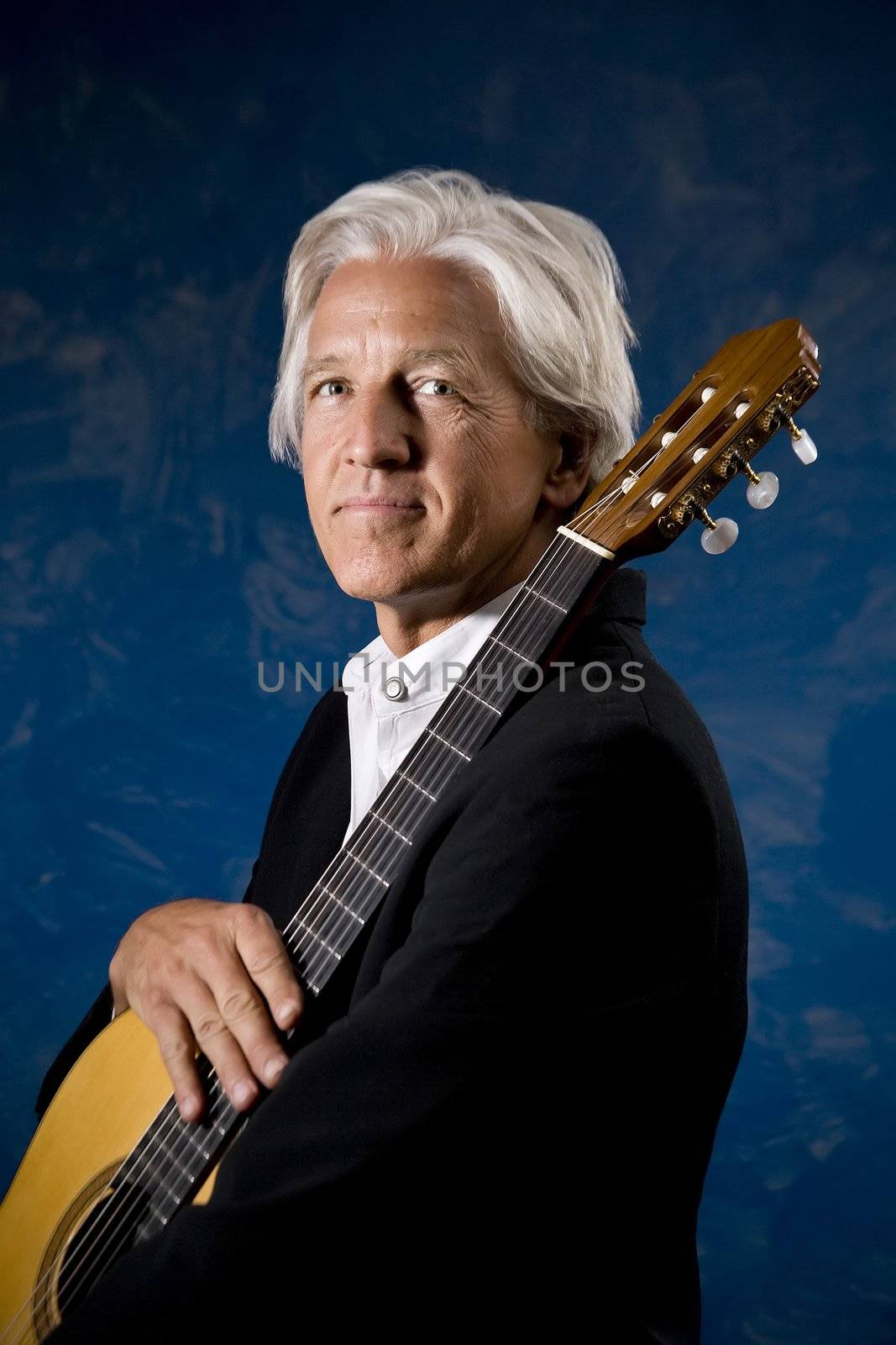 Classical Guitarist with his Instrument in front of a Blue Wall