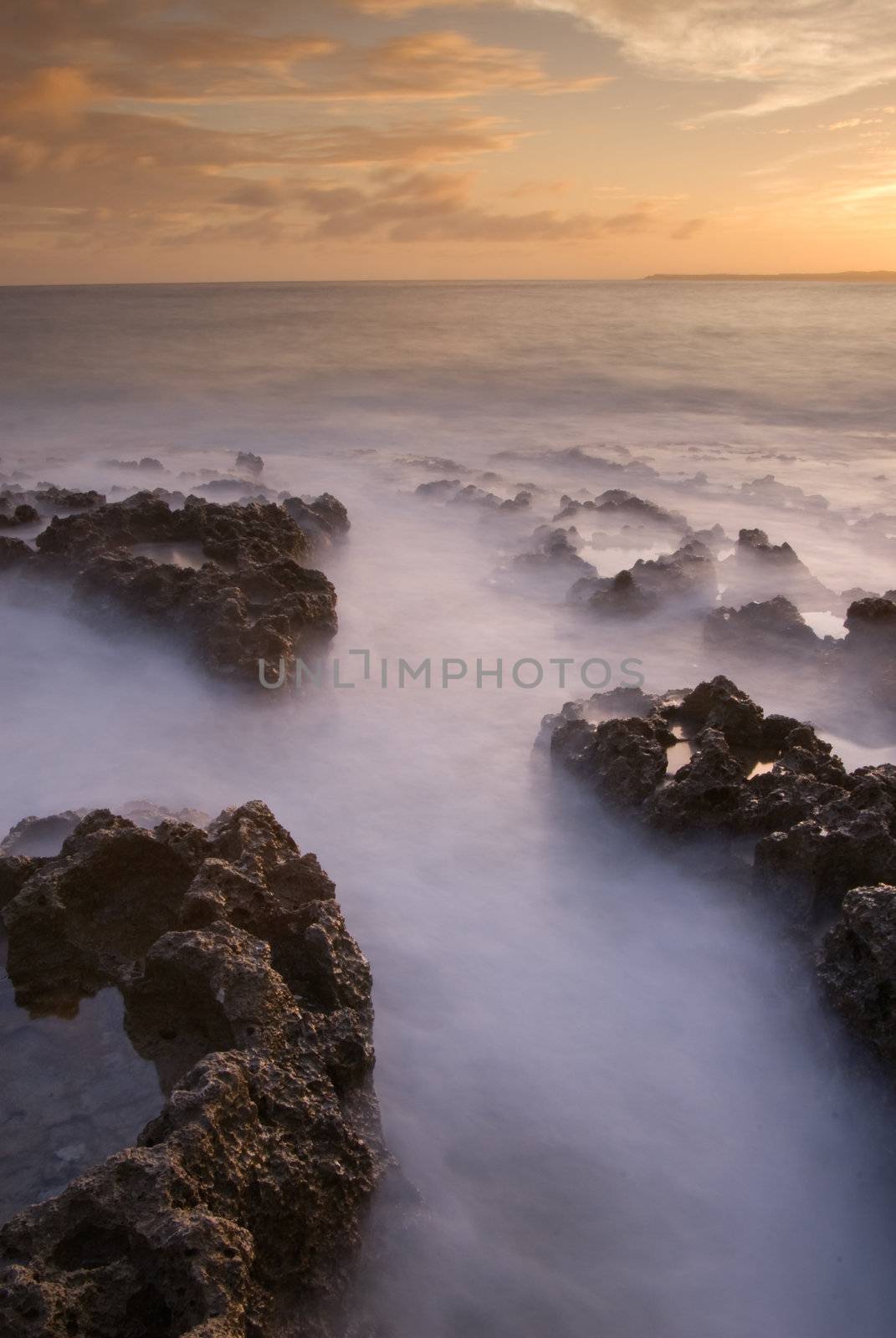 Landscape of sea with dramatic wave and rock in sunset.