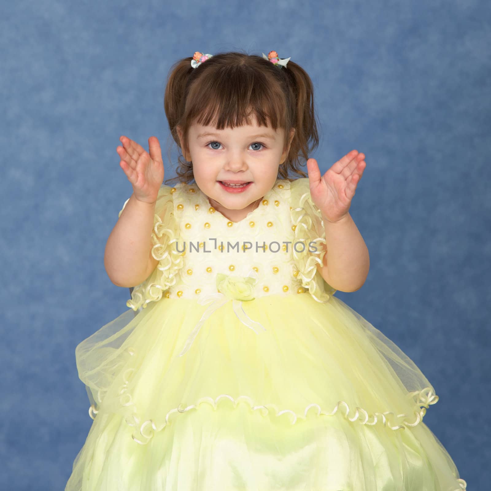 The little girl in a beautiful dress claps his hands on a blue background