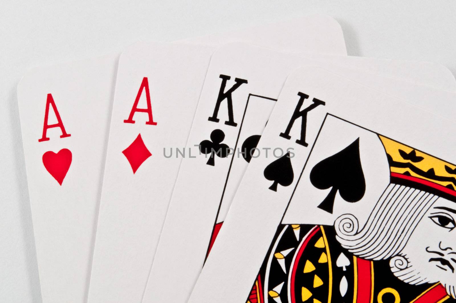 Close up on the top halves of two ace and two king playing cards overlaying one another on a white surface.