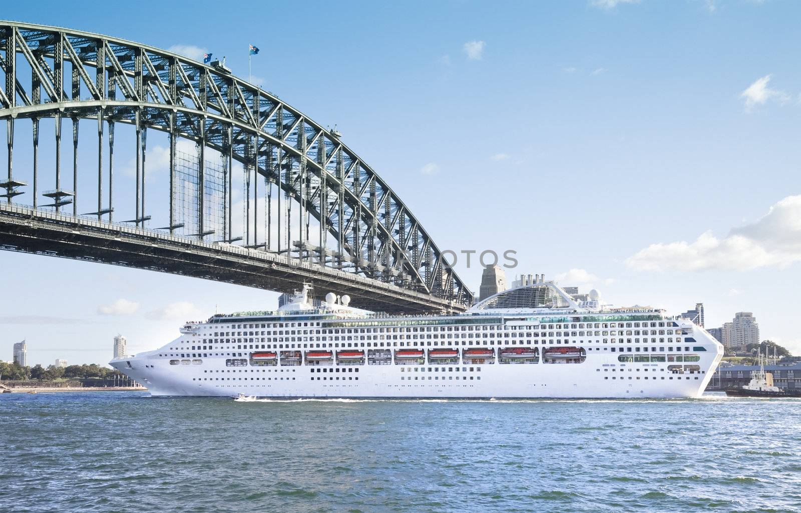 A photography of a cruise ship passing Sydney Harbour Bridge