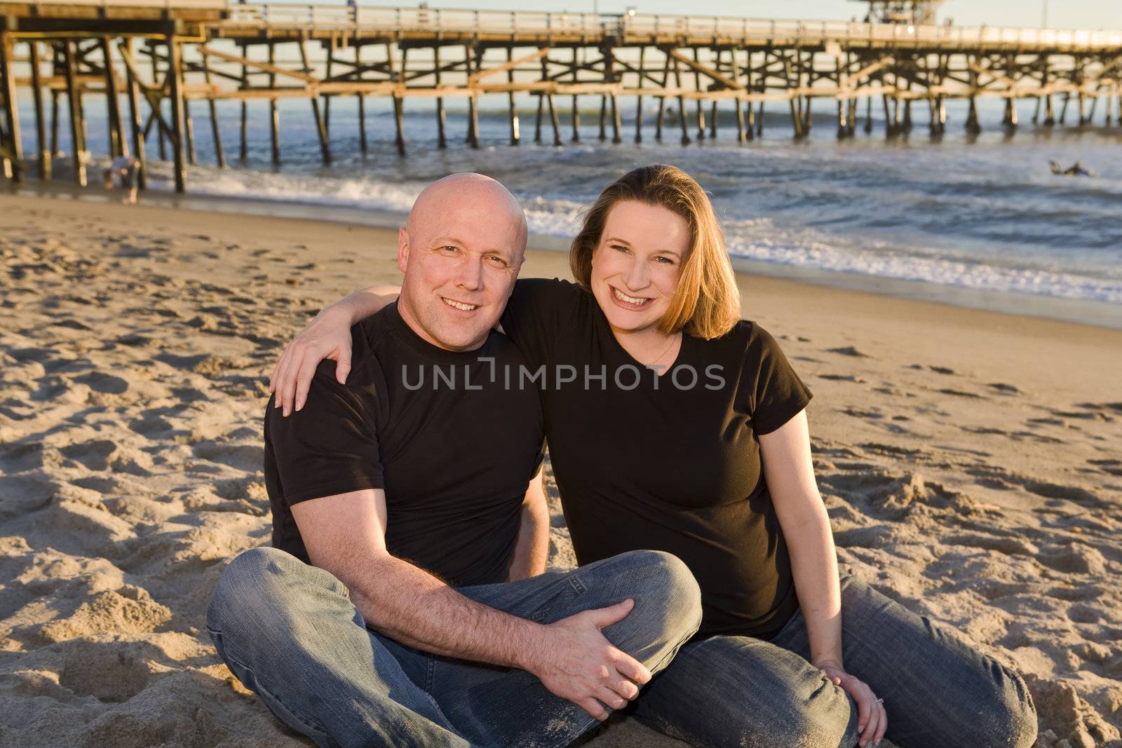 Young Pregnant Couple on the Beach with Pier in Background at Sunset
