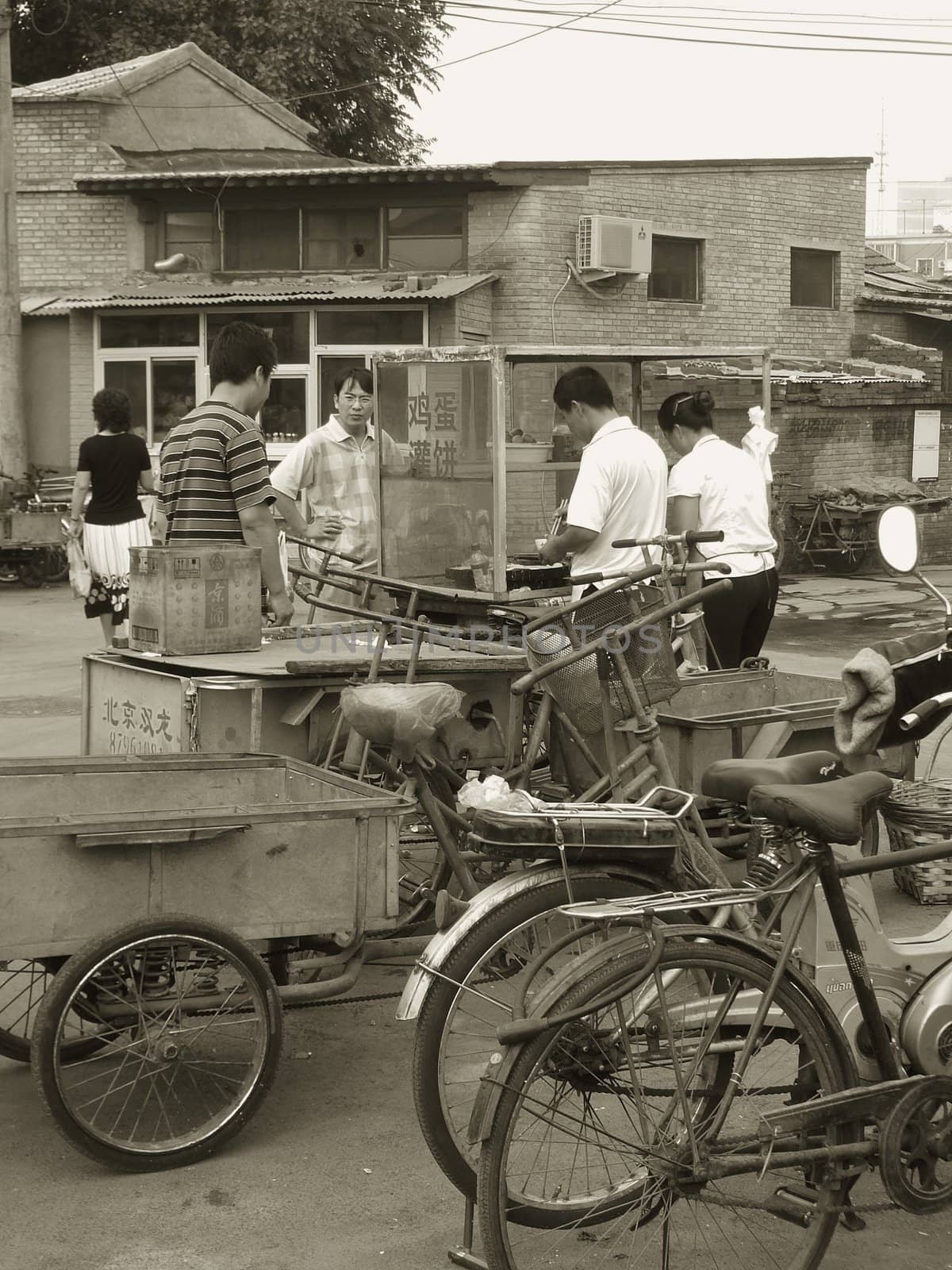 Black and white picture of a typical street scene in China. Before going to work people buy something to eat in a street food shop. This picture was taking in a Beijing hutong (traditional downtown ancient quarter)